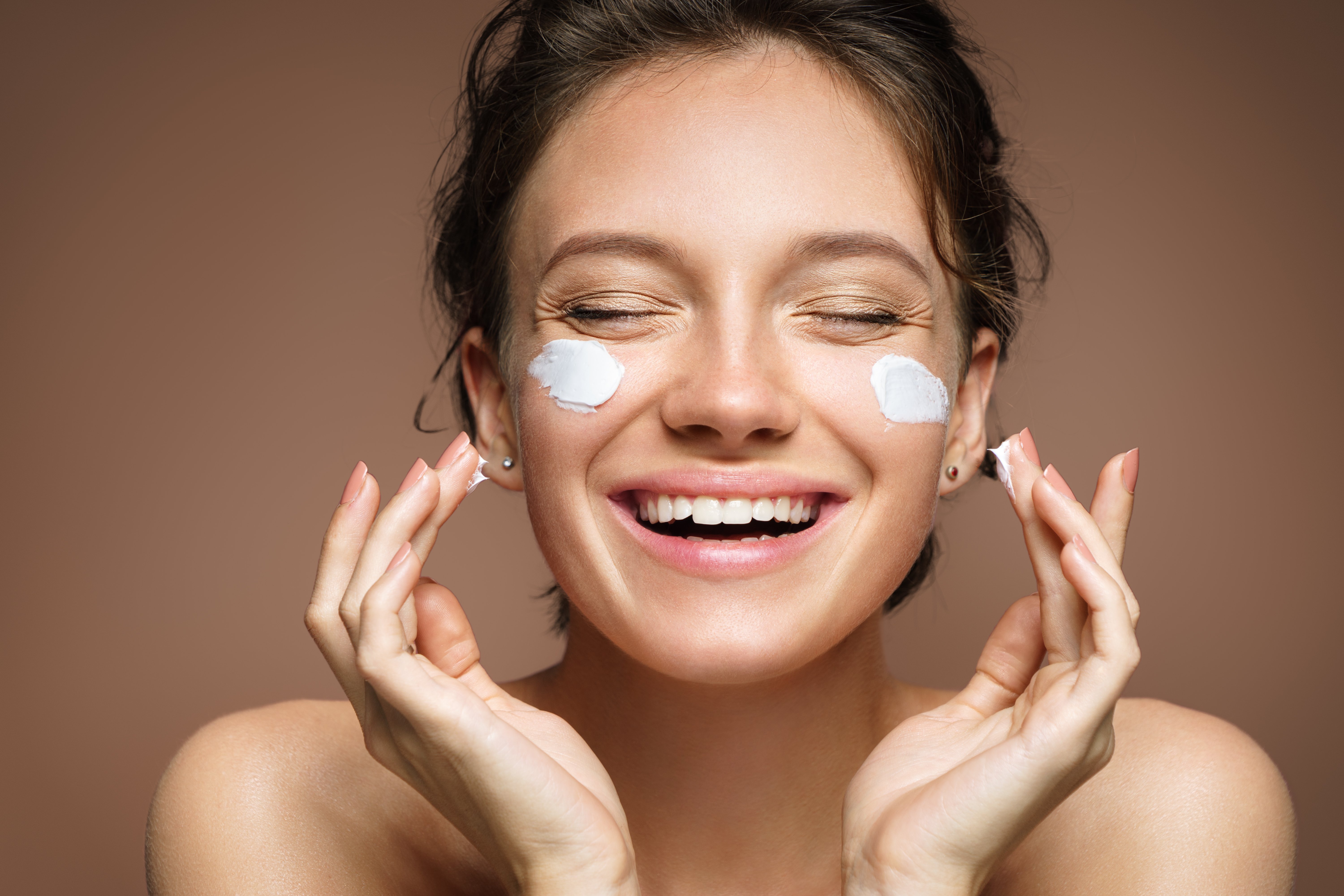 Woman smiling while applying moisturizer. | Source: Shutterstock