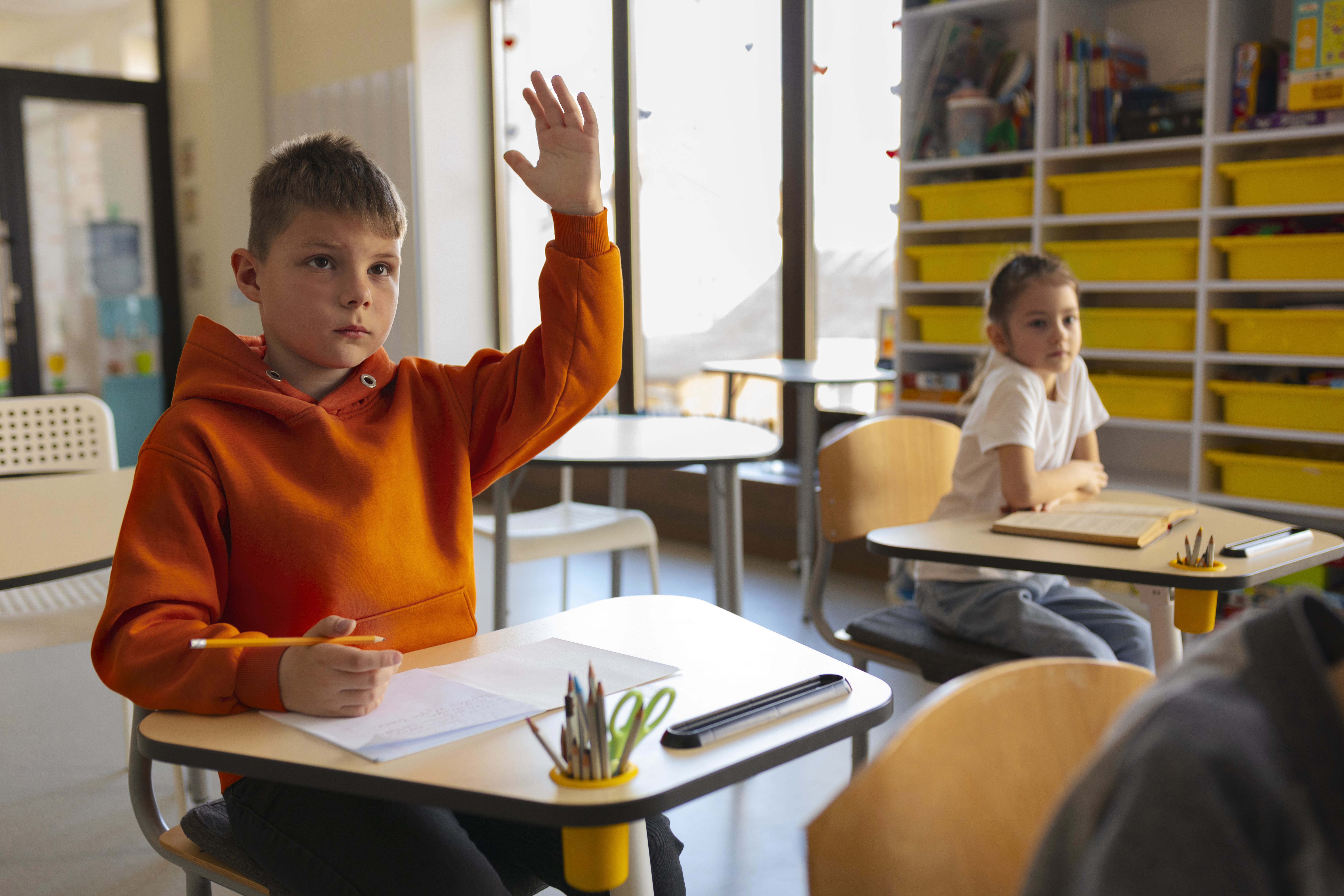 A young boy putting his hand up in class. | Source: freepik