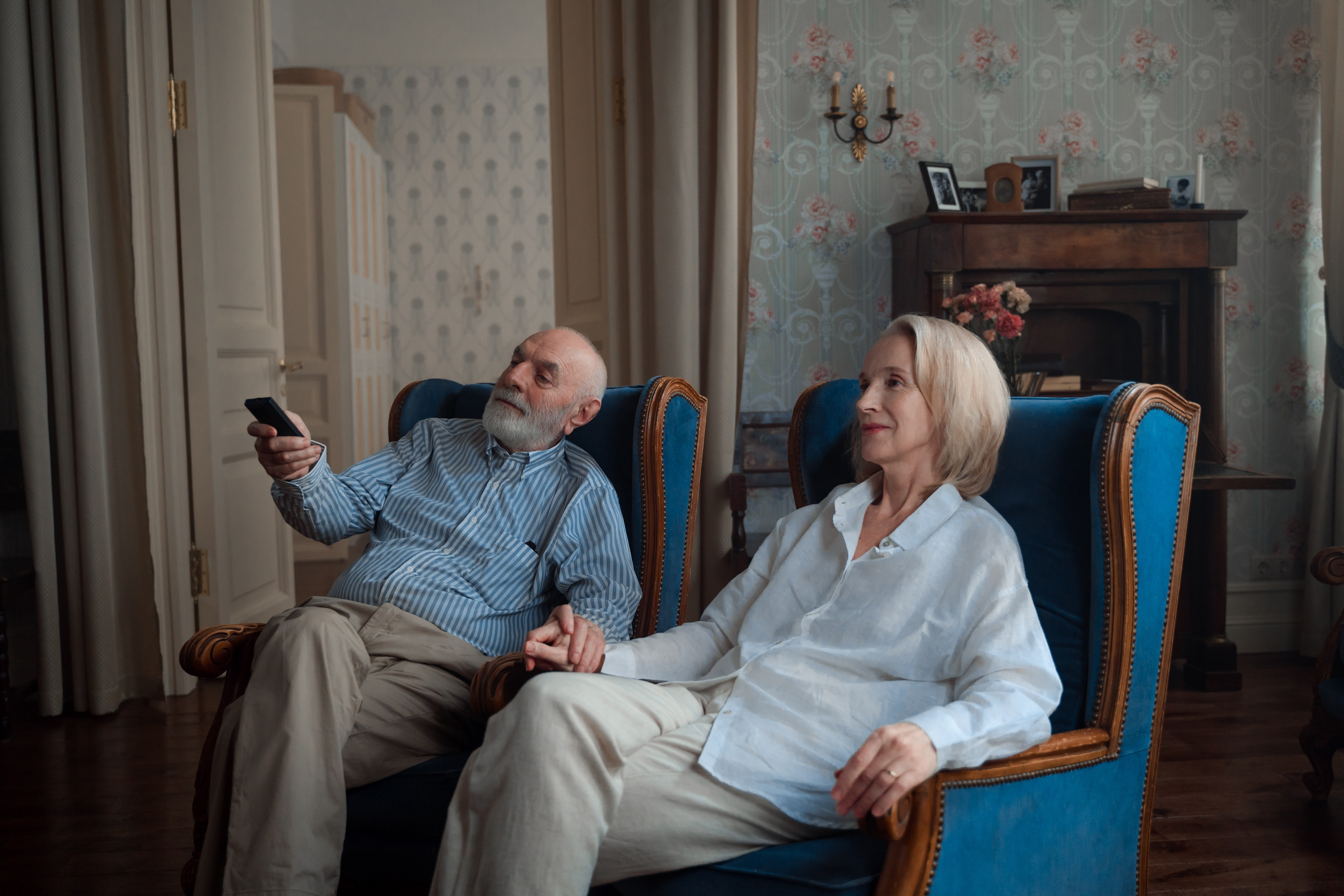 Una pareja mayor sentada cómodamente en poltronas mientras ve televisión en su lujosa sala. | Foto: Pexels