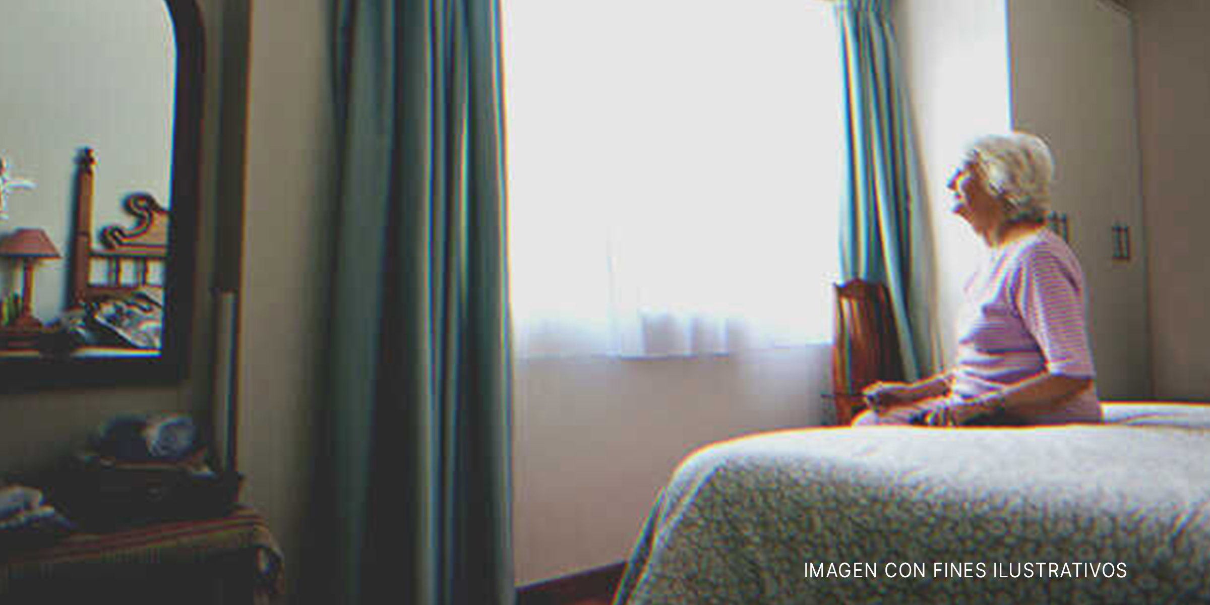 Señora mayor sentada sobre la cama frente a una ventana. | Foto: Shutterstock