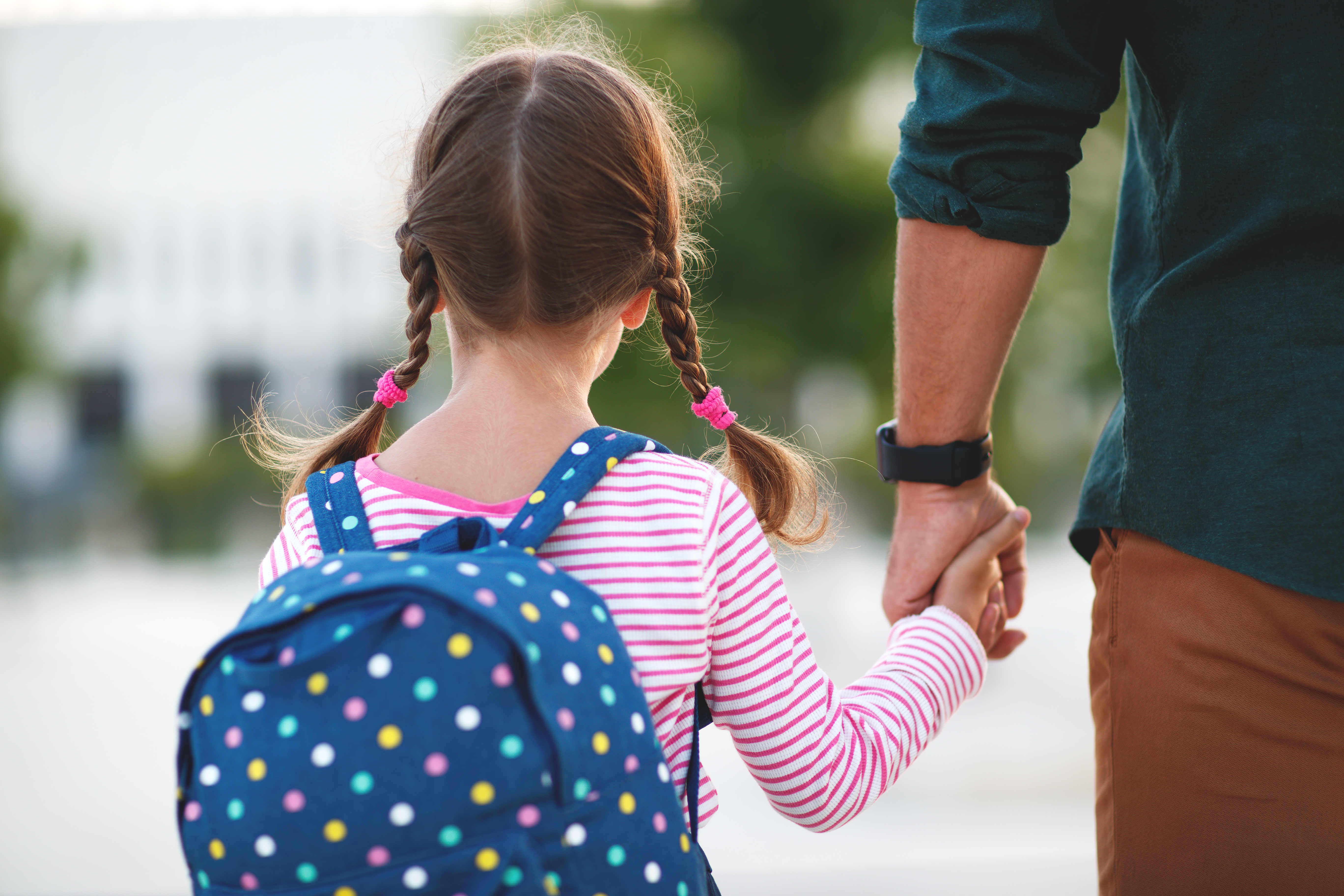 A little girl holds her father's hand while going to school | Source: Shutterstock