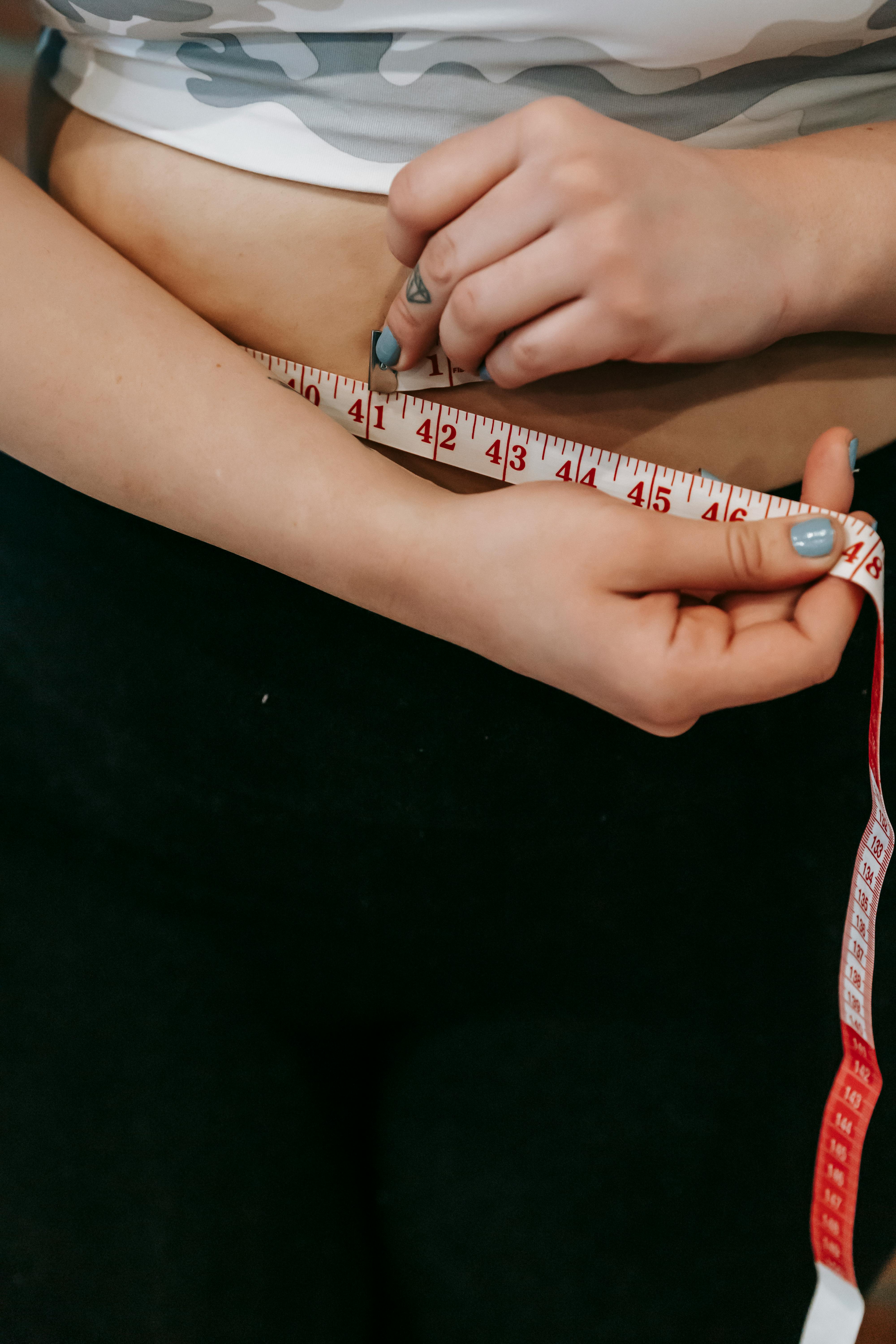 Woman checking waist size with measuring tape | Source: Pexels
