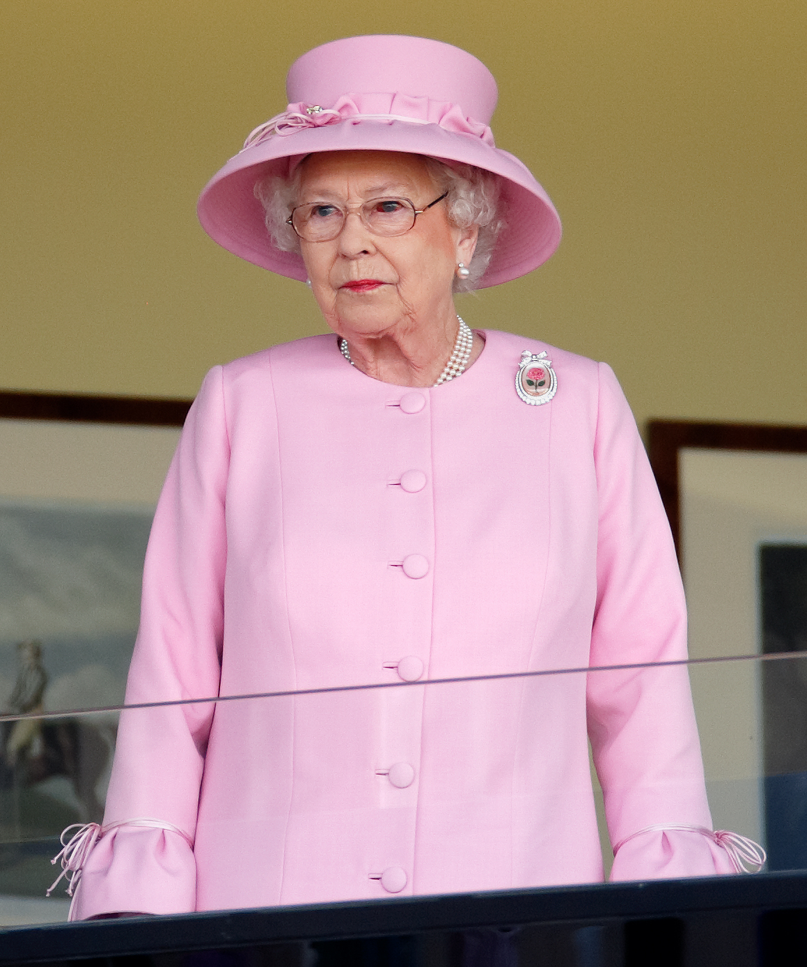 Watching the races from the Royal Box, Queen Elizabeth II is seen with a bloodshot eye while wearing pearls and the Centenary Rose Brooch. Her poised expression reflects duty, even amid a visible burst vessel during the high-society gathering.