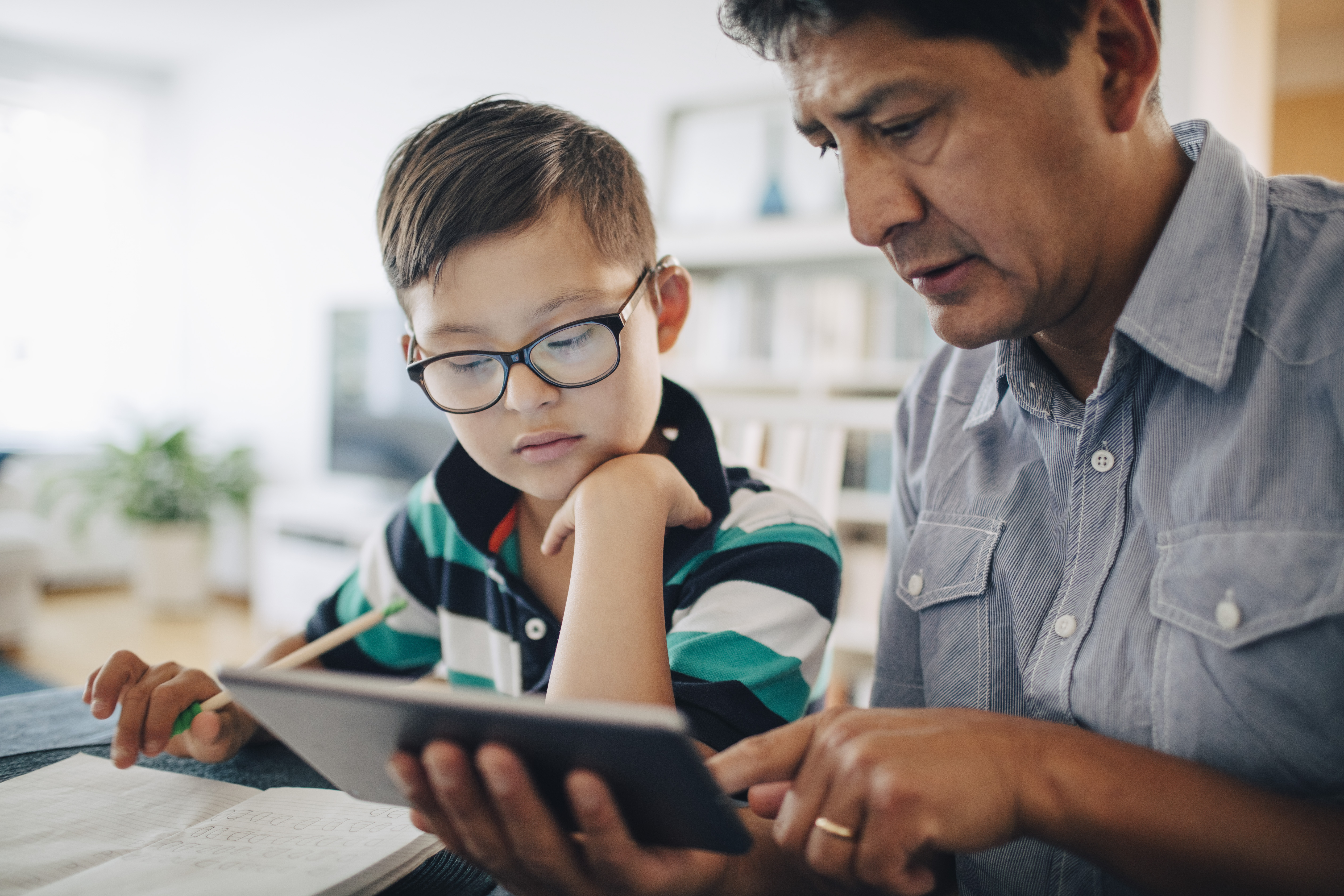 Father showing digital tablet to son while studying at table | Source: Getty Images