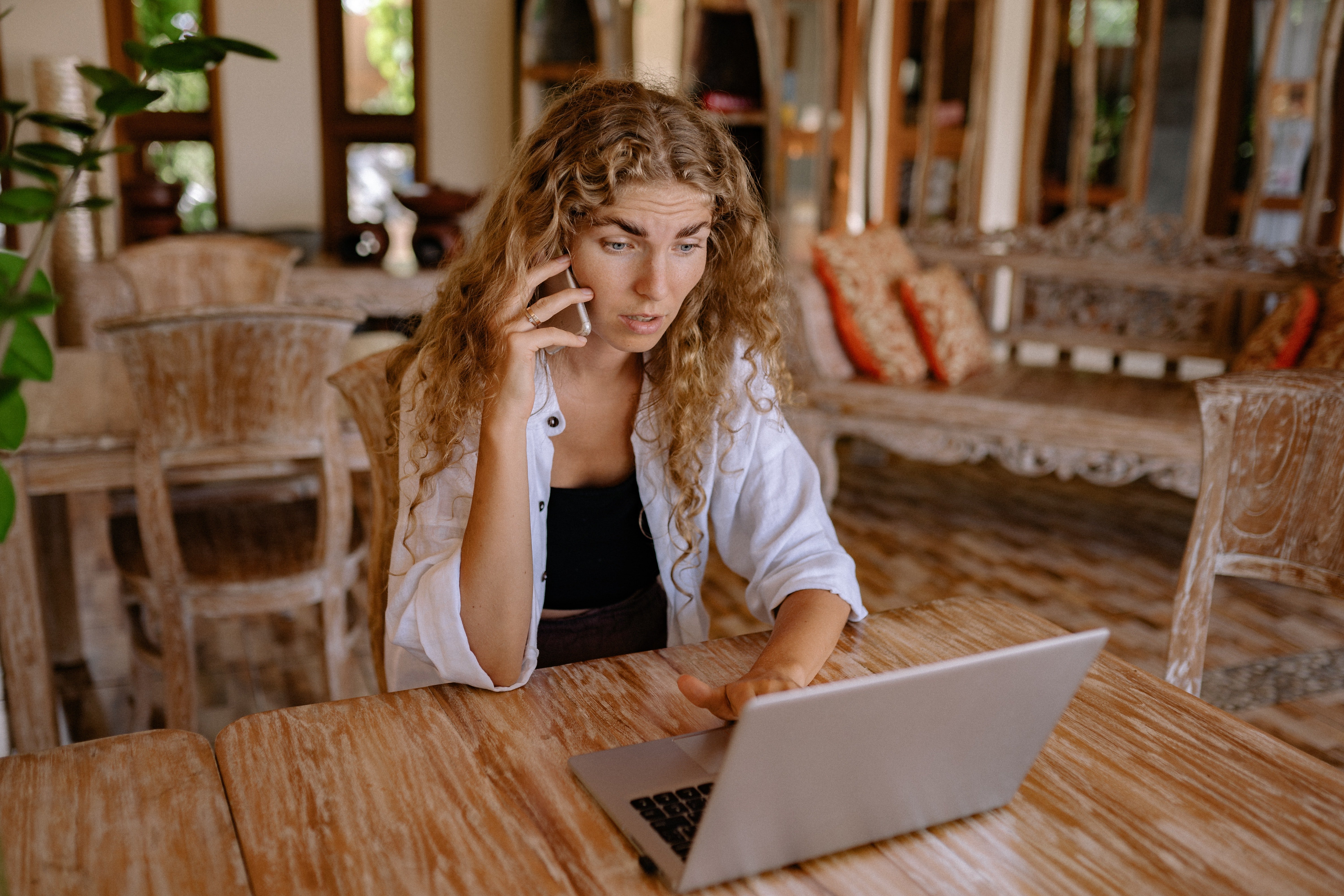 Mujer frente a una computadora hablando a través de un teléfono celular. | Foto: Pexels