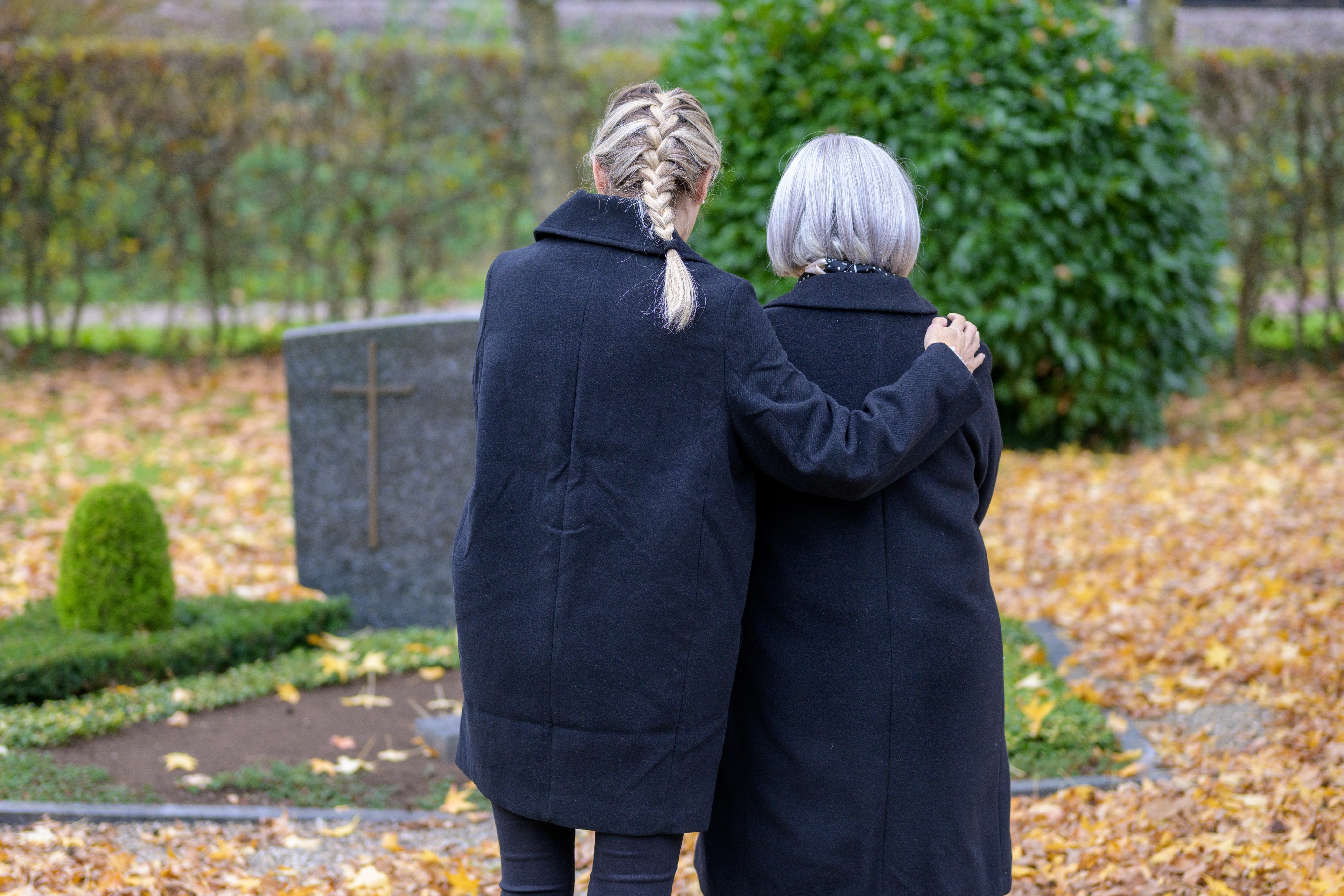Two women at the man's grave in the cemetery on a cloudy cold day. | Source: Shutterstock