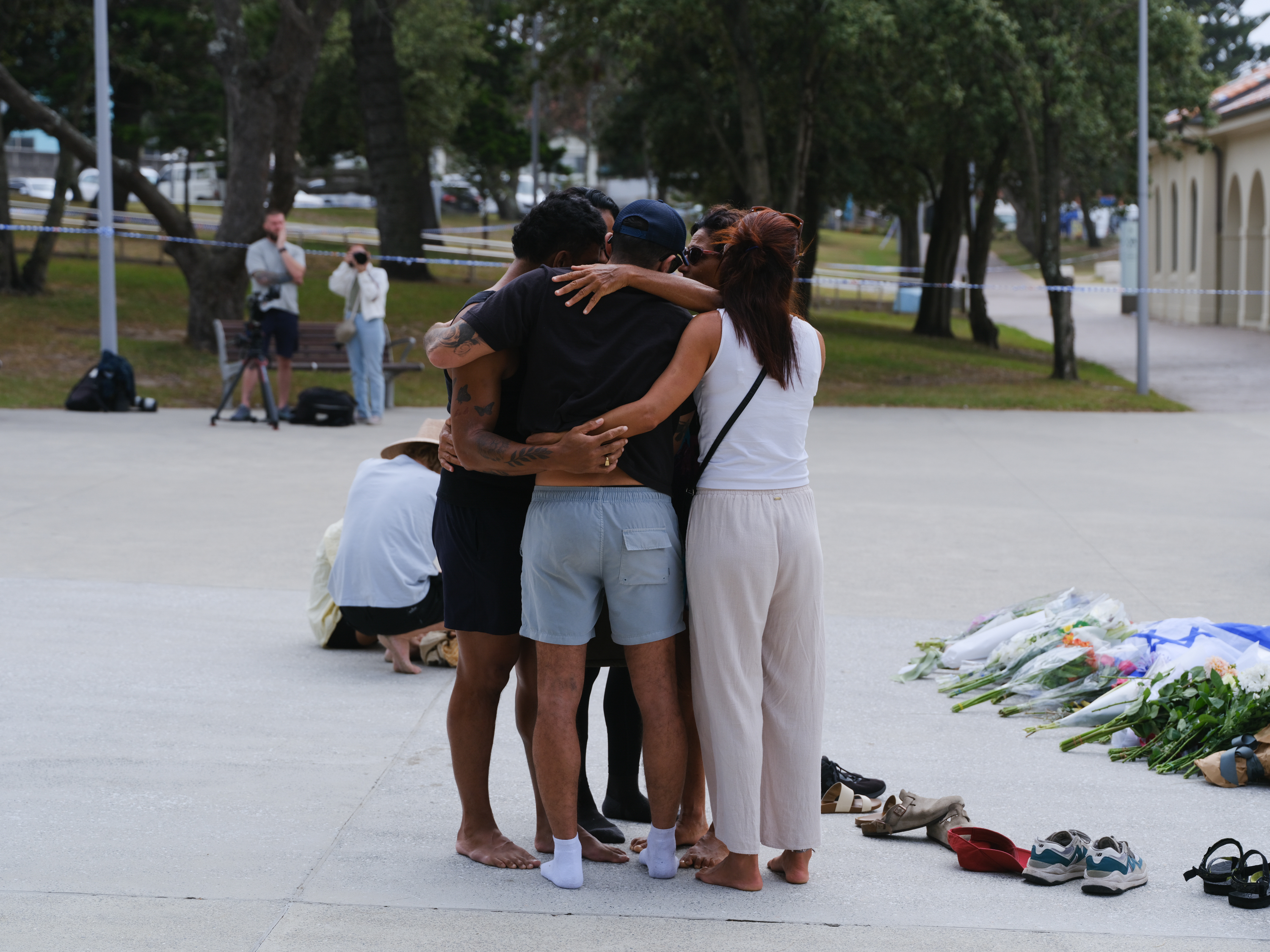 Mourners embraced near a growing sea of floral tributes left for the victims of the Bondi Beach shooting. Pairs of shoes, candles, and handwritten notes lay scattered on the pavement — quiet markers of a community united in sorrow and solidarity.