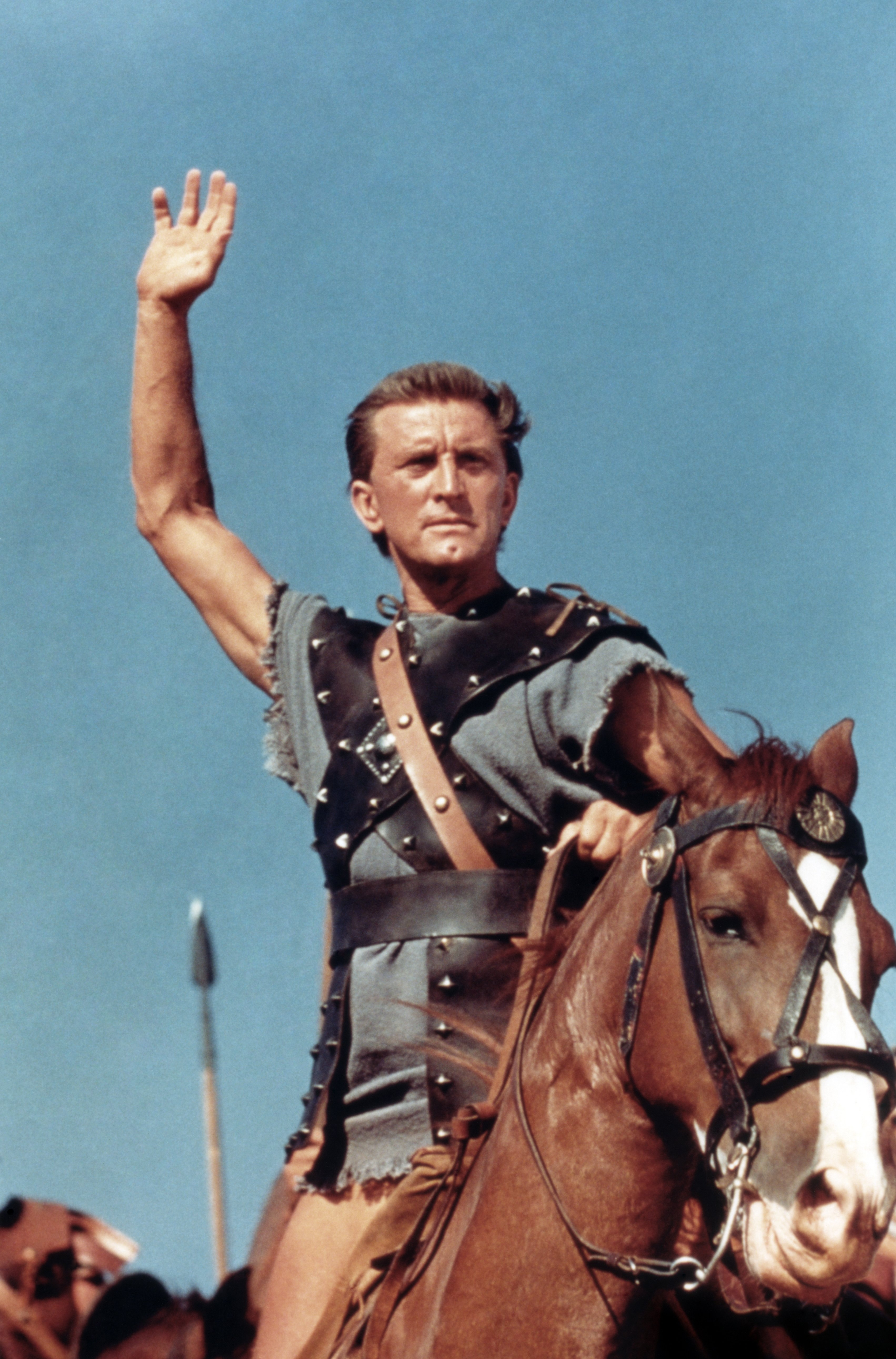 Kirk Douglas in the 1960 action film "Spartacus" pictured on top of a horse with his hand raised in the air. / Source: Getty Images