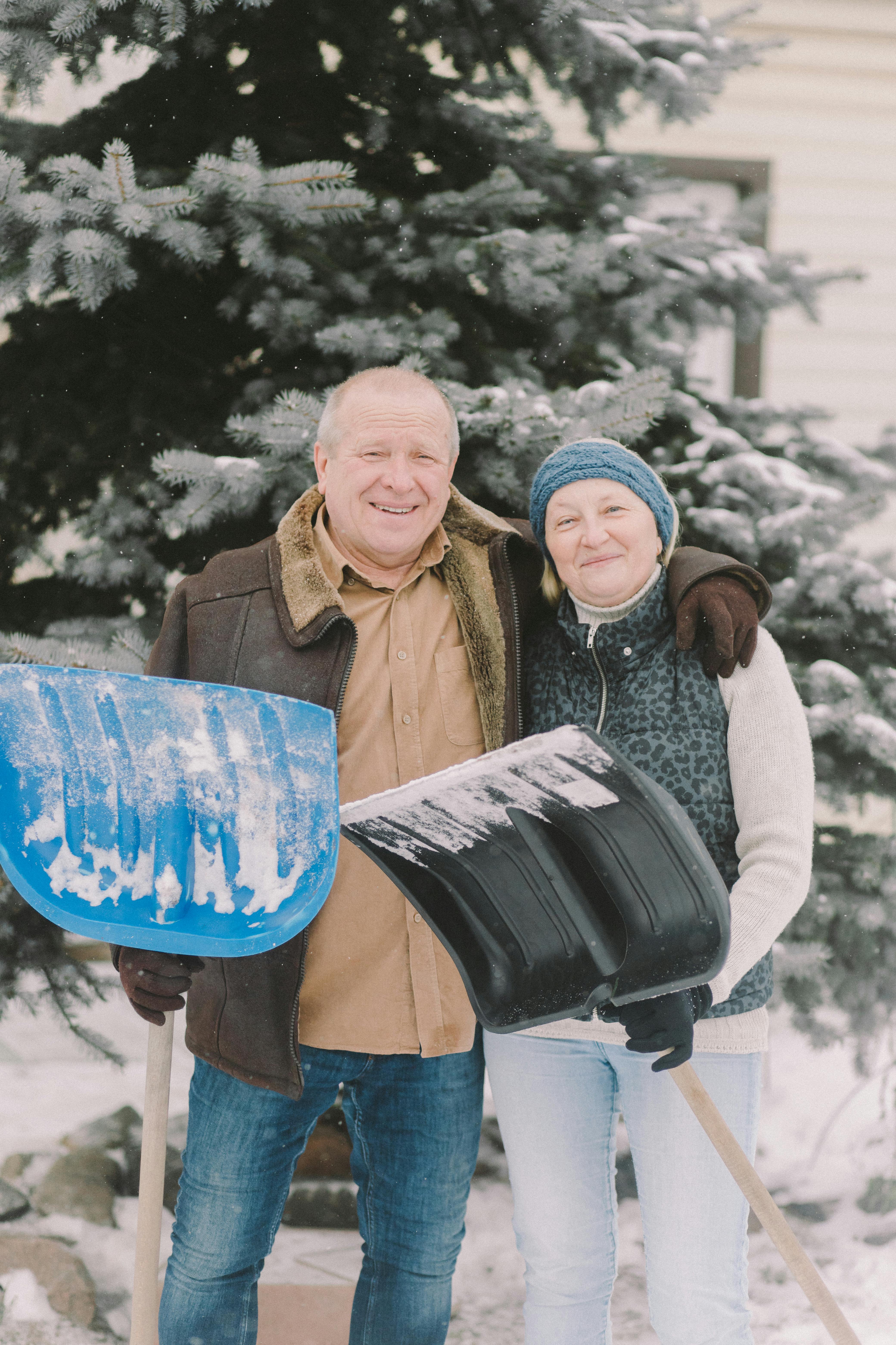A happy middle-aged couple embracing while holding snow shovels | Source: Pexels