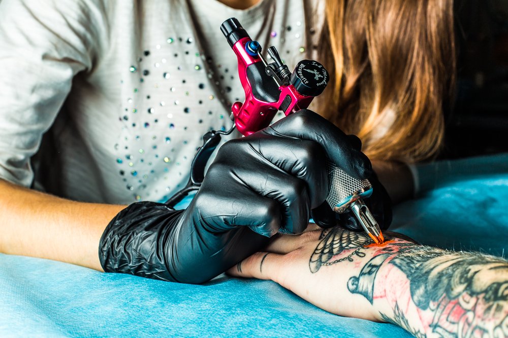 Tatuadora tatuando la mano de un cliente. | Foto: Shutterstock