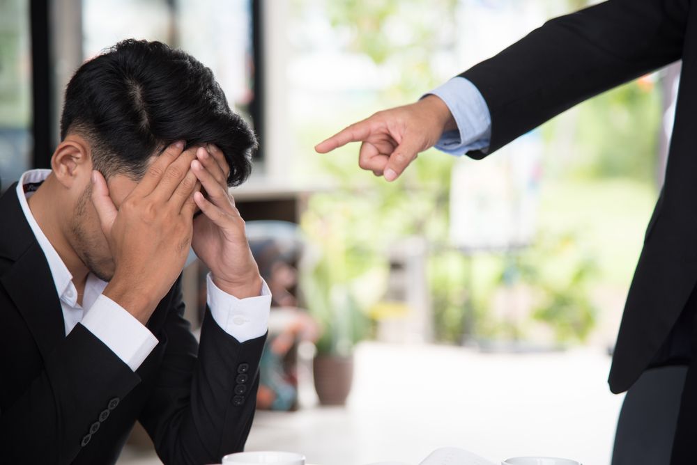 A problematic man sits on the ground while another man points at him | Photo: Shutterstock