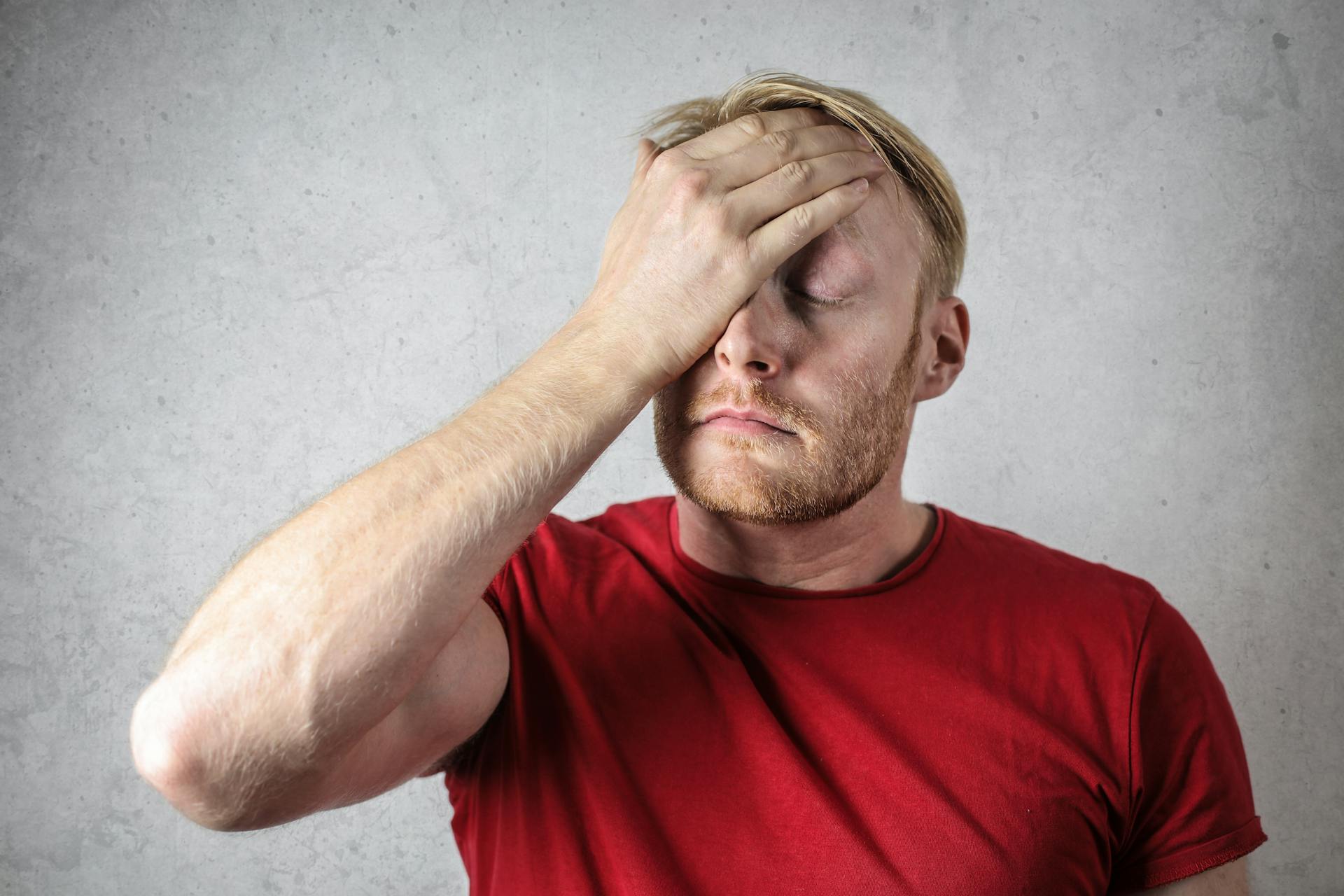 An annoyed man in red T-shirt covering his face | Source: Pexels