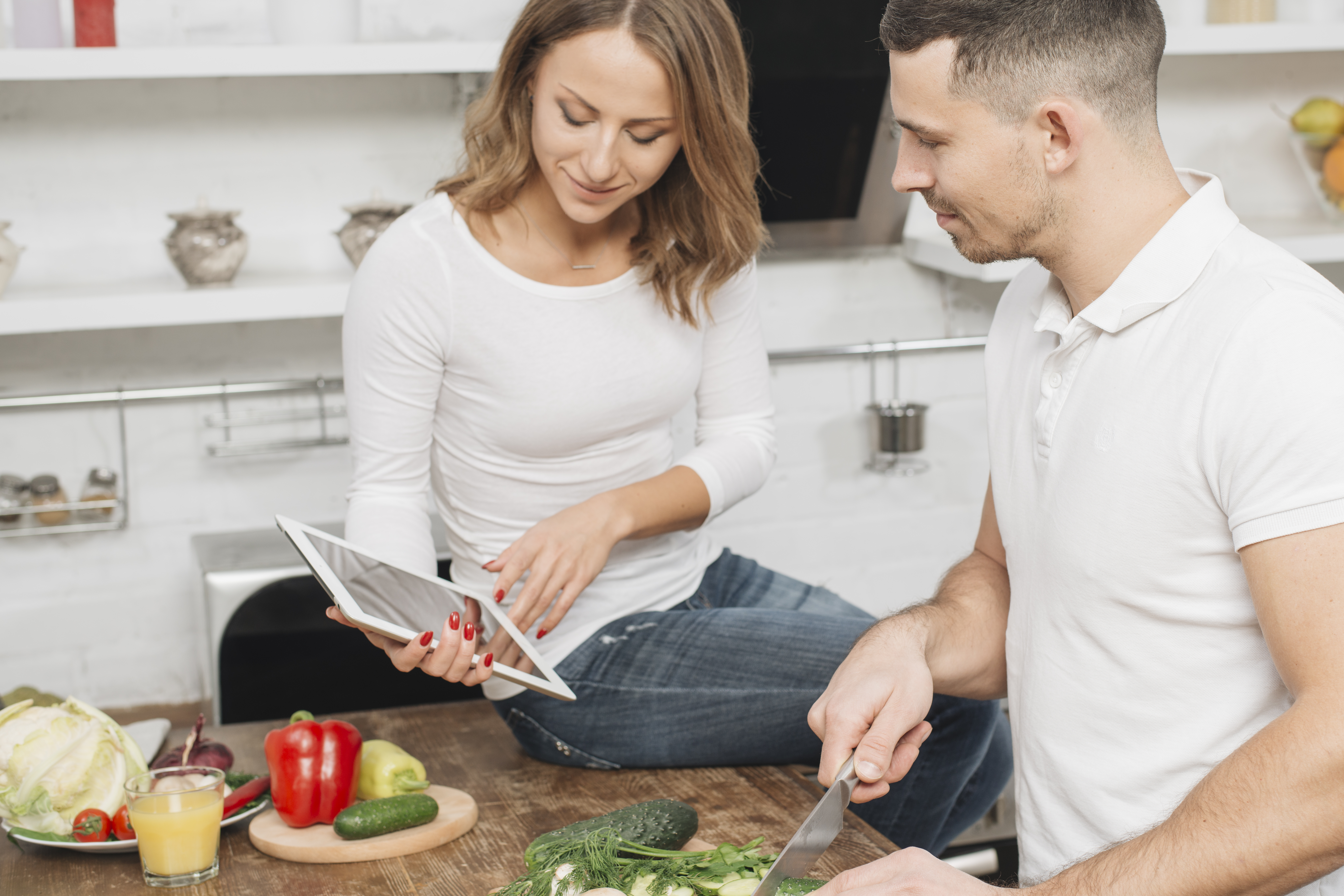 Woman showing a tablet to a man while cooking in the kitchen | Source: Freepik