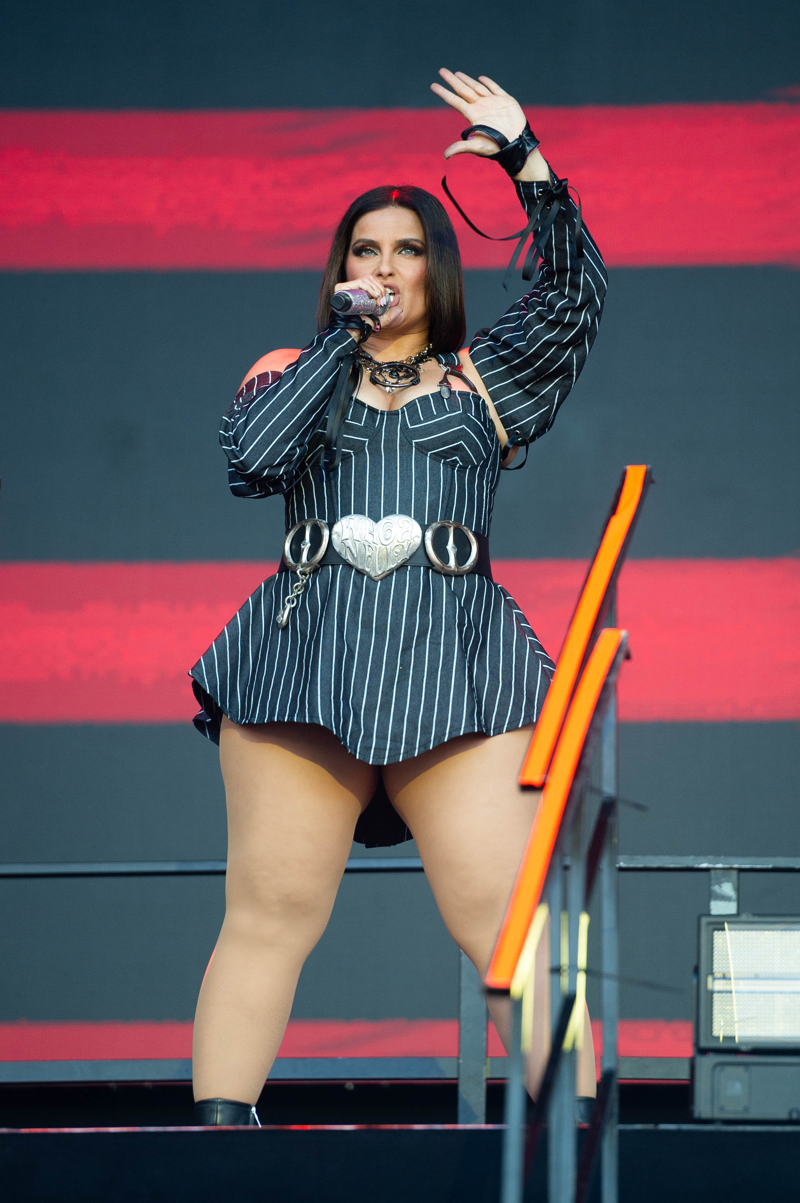 Nelly Furtado commands the stage at the Superbloom Festival in Munich, Bavaria, performing in a bold black striped outfit with statement accessories, holding a microphone mid-performance as she energizes the crowd against a vibrant backdrop.