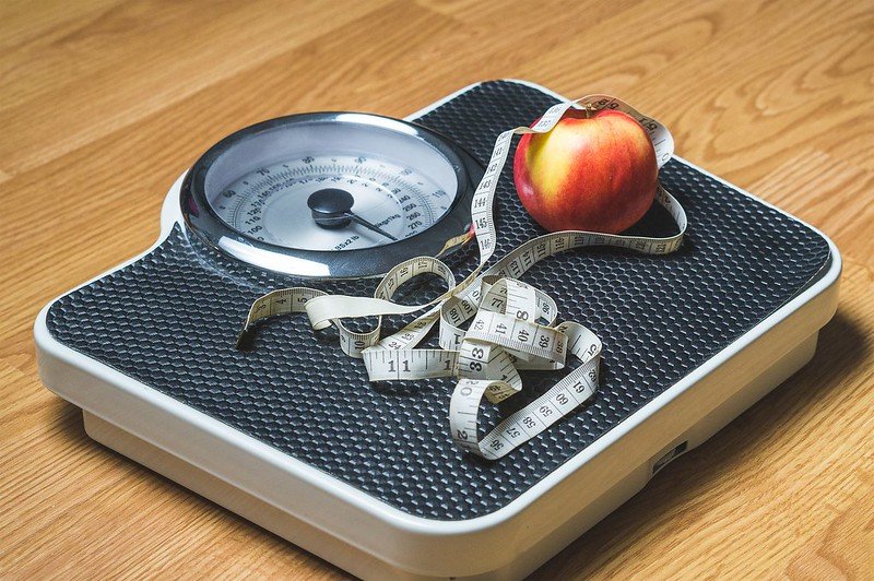 A weighing scale with an apple and a tape rule on it. | Photo:Flickr