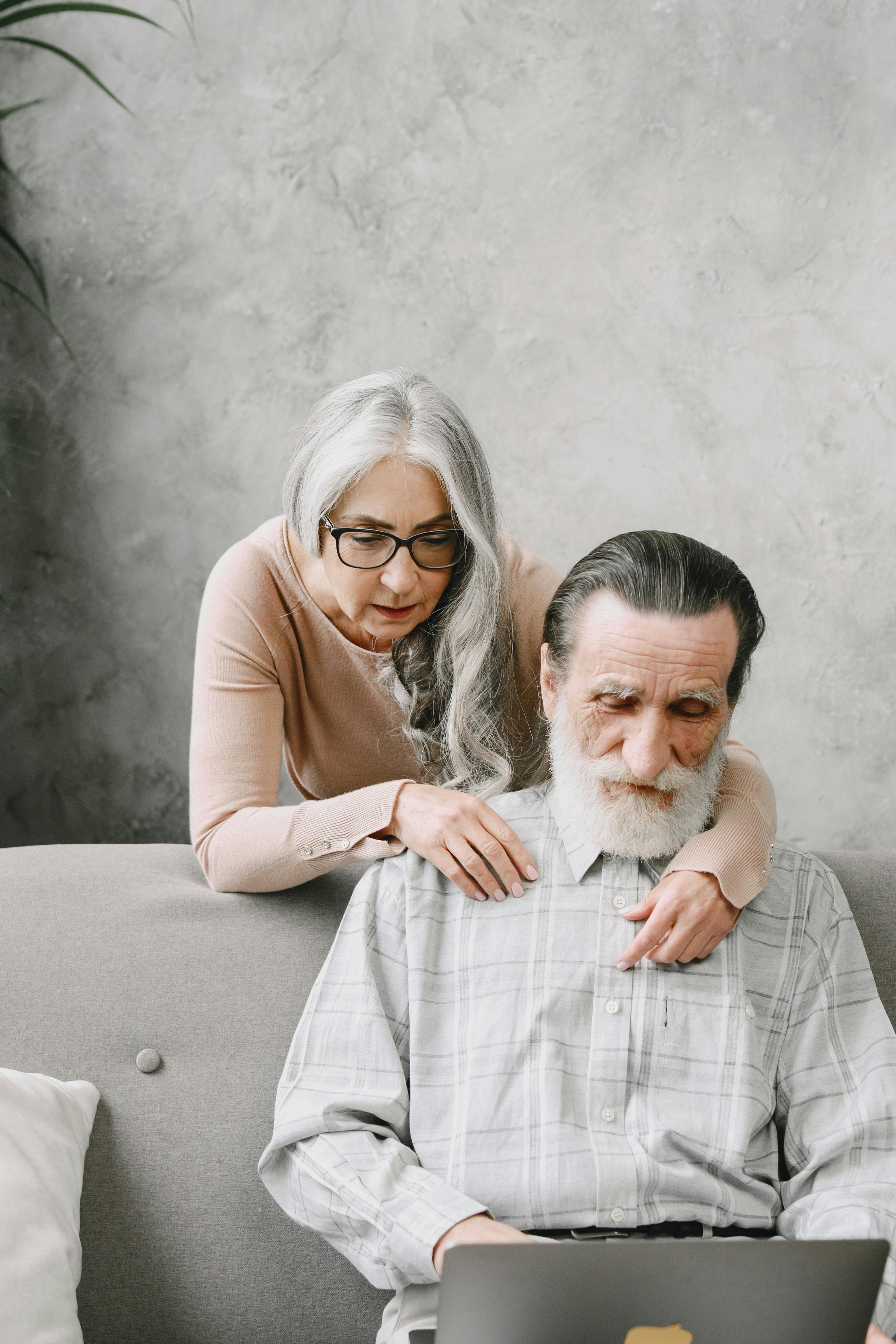 A woman looks over a man's shoulder as they use a laptop together at home. | Source: Pexels