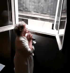 La señora Charo mira por la ventana emocionada a todos los vecinos que la felicitan. | Foto: Captura de Twitter/eldiarioes