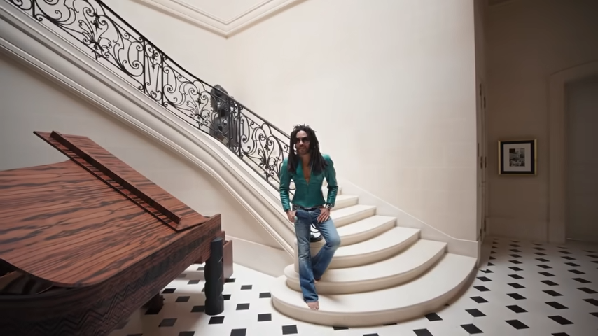 Lenny Kravitz poses barefoot on his grand limestone staircase, clad in a turquoise leather jacket next to his custom-designed Steinway. | Source: YouTube/@Archdigest