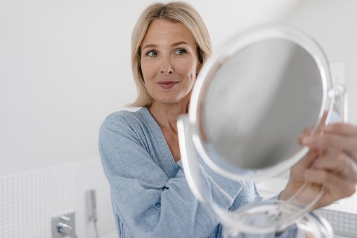 Une femme mûre se regarde dans un miroir de beauté dans la salle de bains | Photo : Getty Images