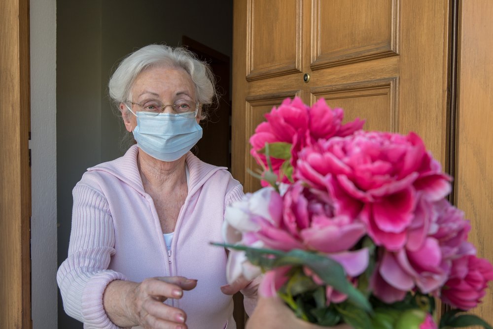 A senior woman wearing a protective face mask receives flowers at her door on Mother's day | Photo: Shutterstock/Gulliver20