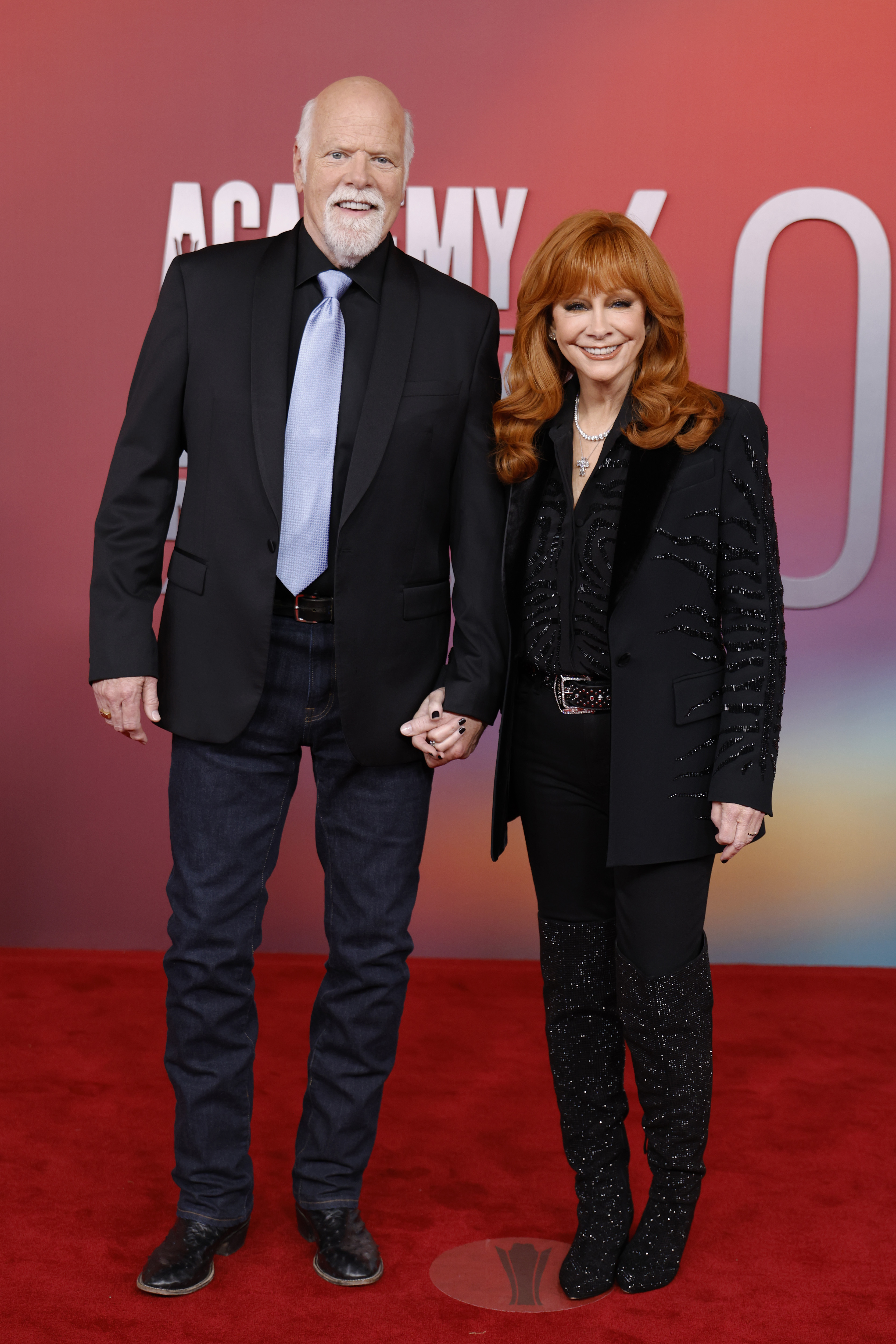 Reba McEntire rocks glittering knee-high boots and a velvet-trimmed blazer, while Rex Linn keeps it sharp in a black jacket and periwinkle tie on the red carpet