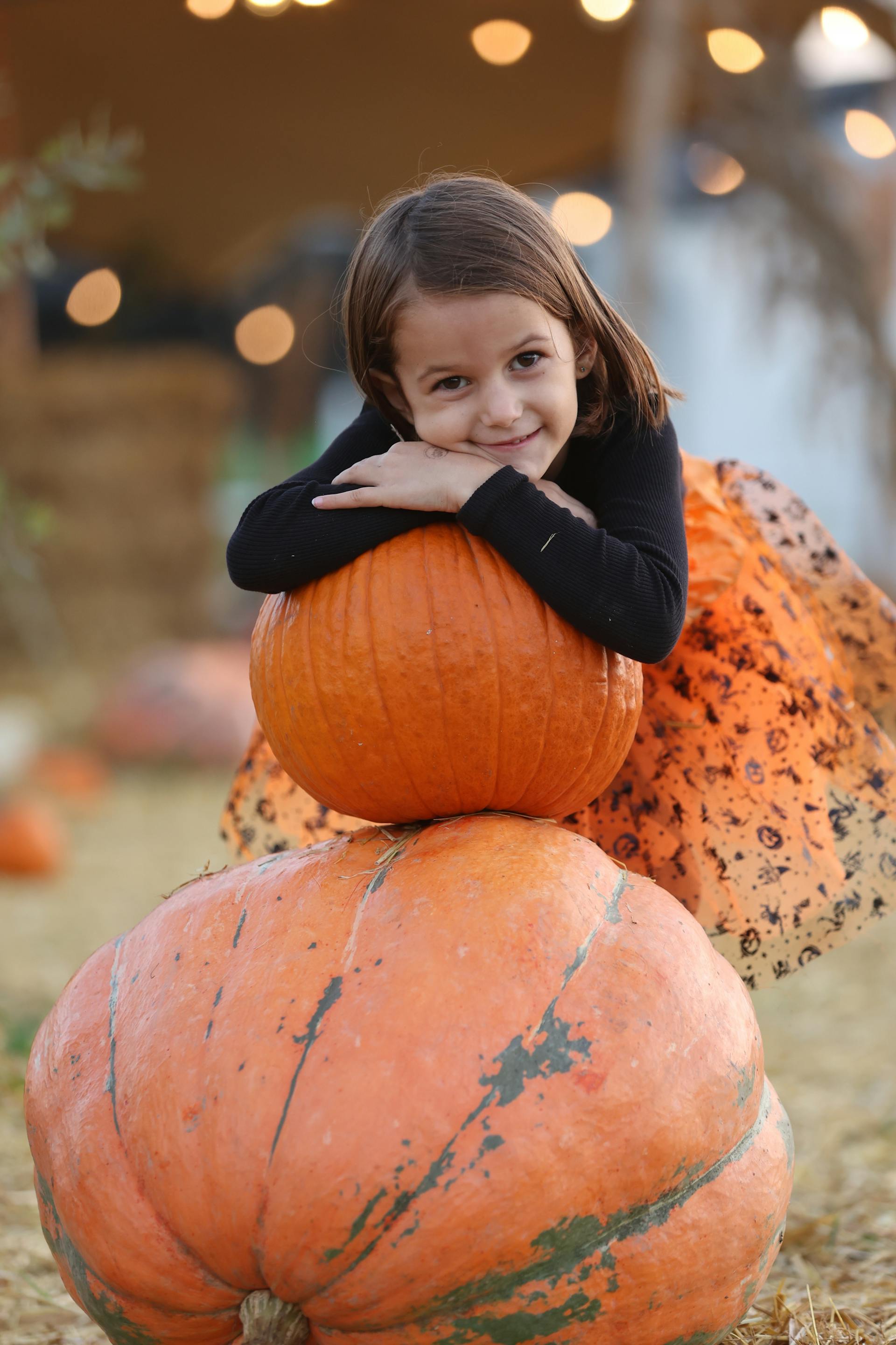 A little girl resting her head on top of a stack of pumpkins | Source: Pexels