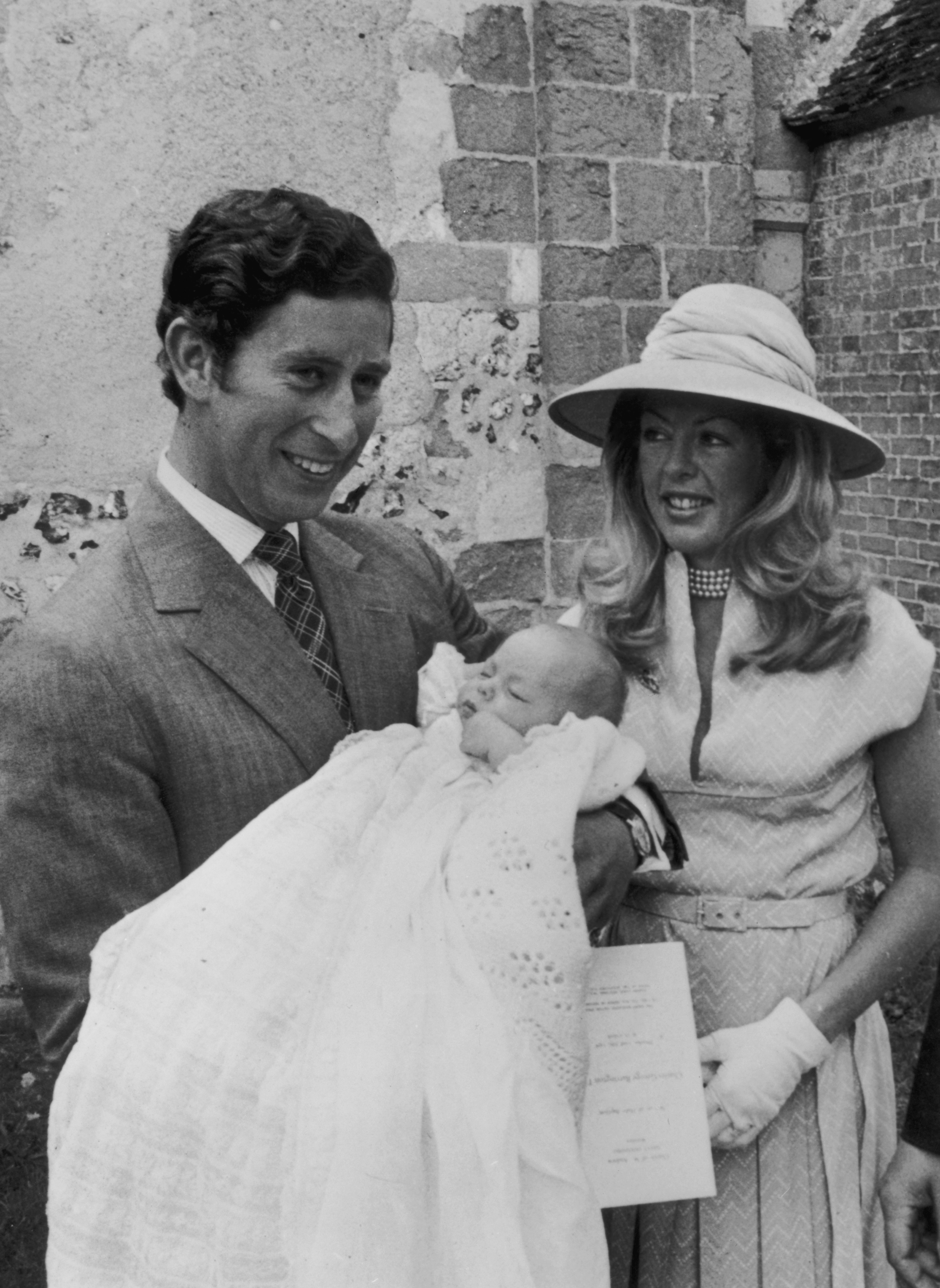 Prince Charles standing next to Dale Tryon as he holds his 9-week-old godson, Charles George Barrington Tryon, after the boy's baptism at the Church of St. Andrews, Durnford, Wiltshire, on July 23, 1976 | Source: Getty Images