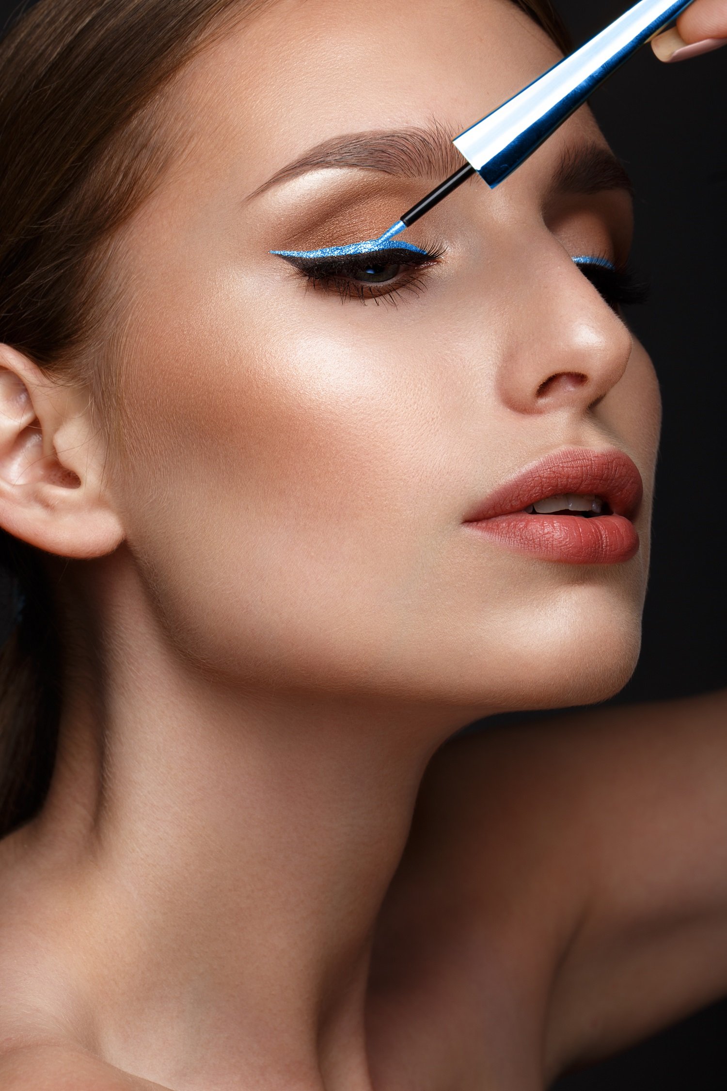 Mujer maquillando sus párpados con un delineador azul brillante. | Foto: Shutterstock