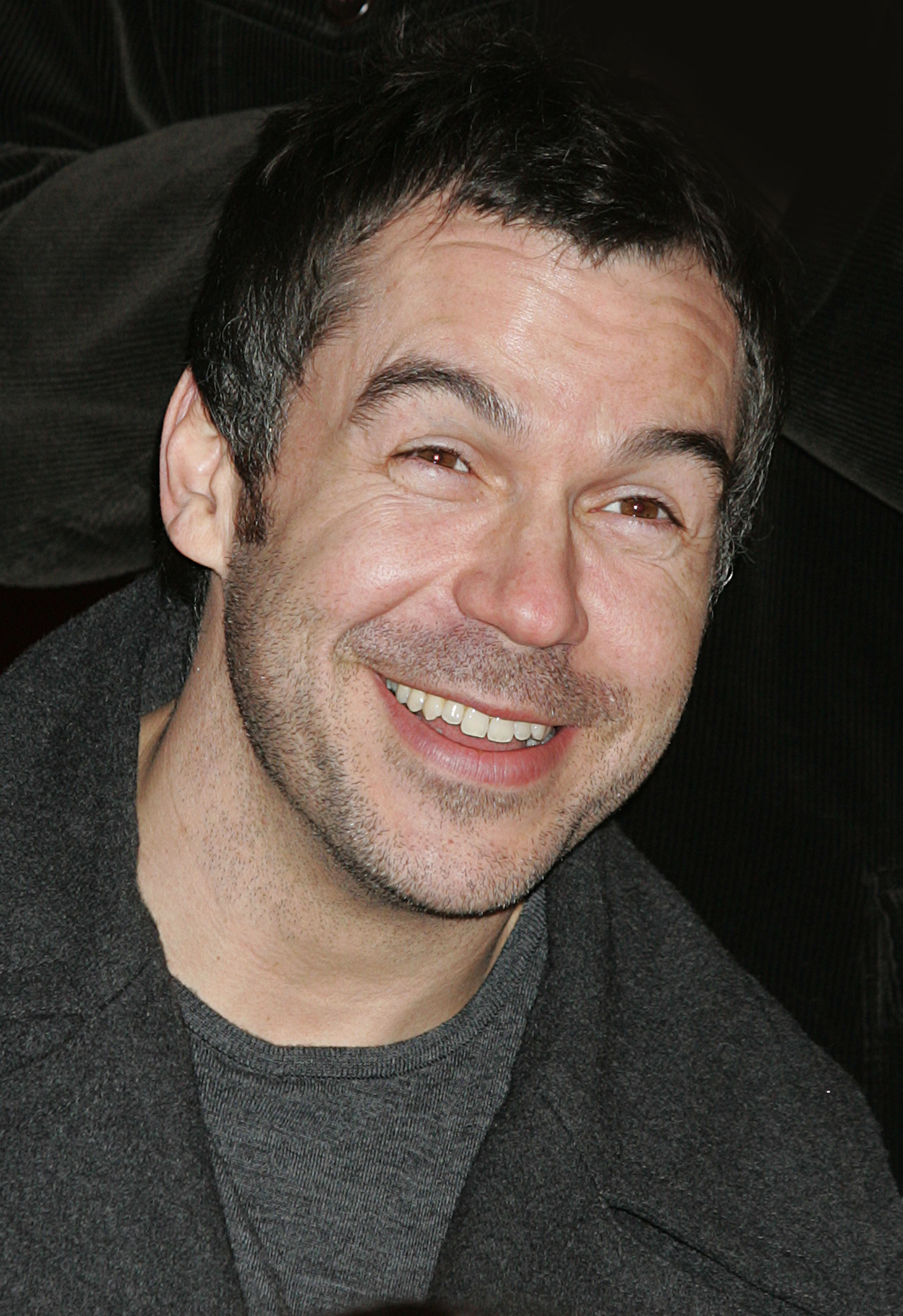 A close-up of Brookstein at a photocall ahead of the first night of the "X Factor Live Tour" at Wembley Arena Pavilion in February 2005, wearing a dark jacket and grinning broadly at the camera, lightly stubbled and visibly at ease.