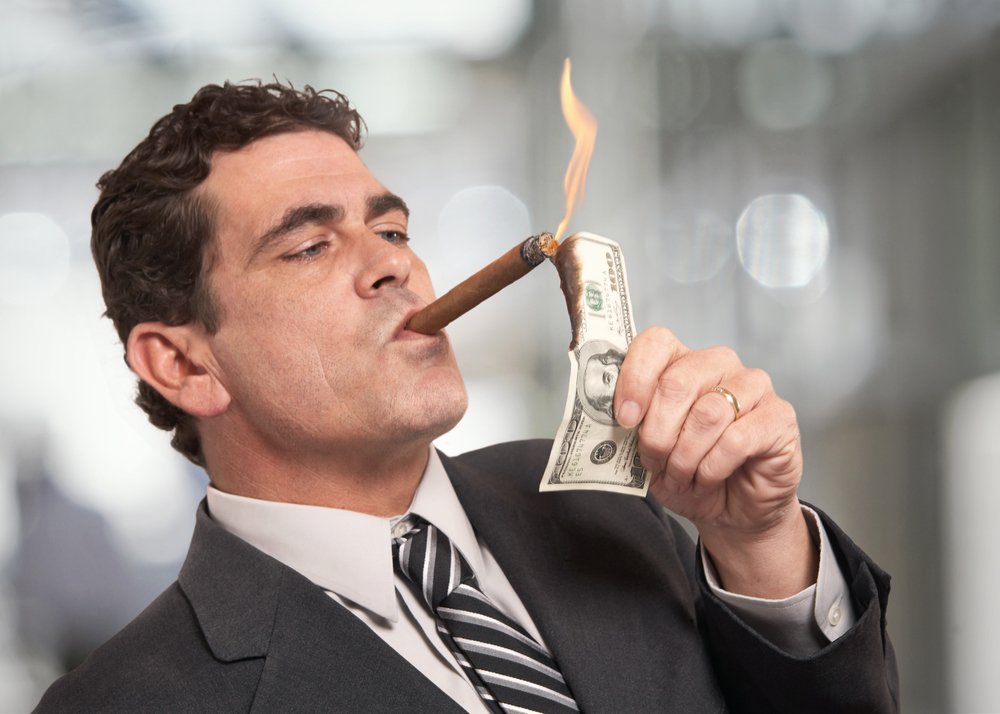 Un riche homme d'affaires qui allume des cigarettes avec un billet de 100 $. | Source : Shutterstock Un riche homme d'affaires qui allume des cigarettes avec un billet de 100 $. | Source : Shutterstock