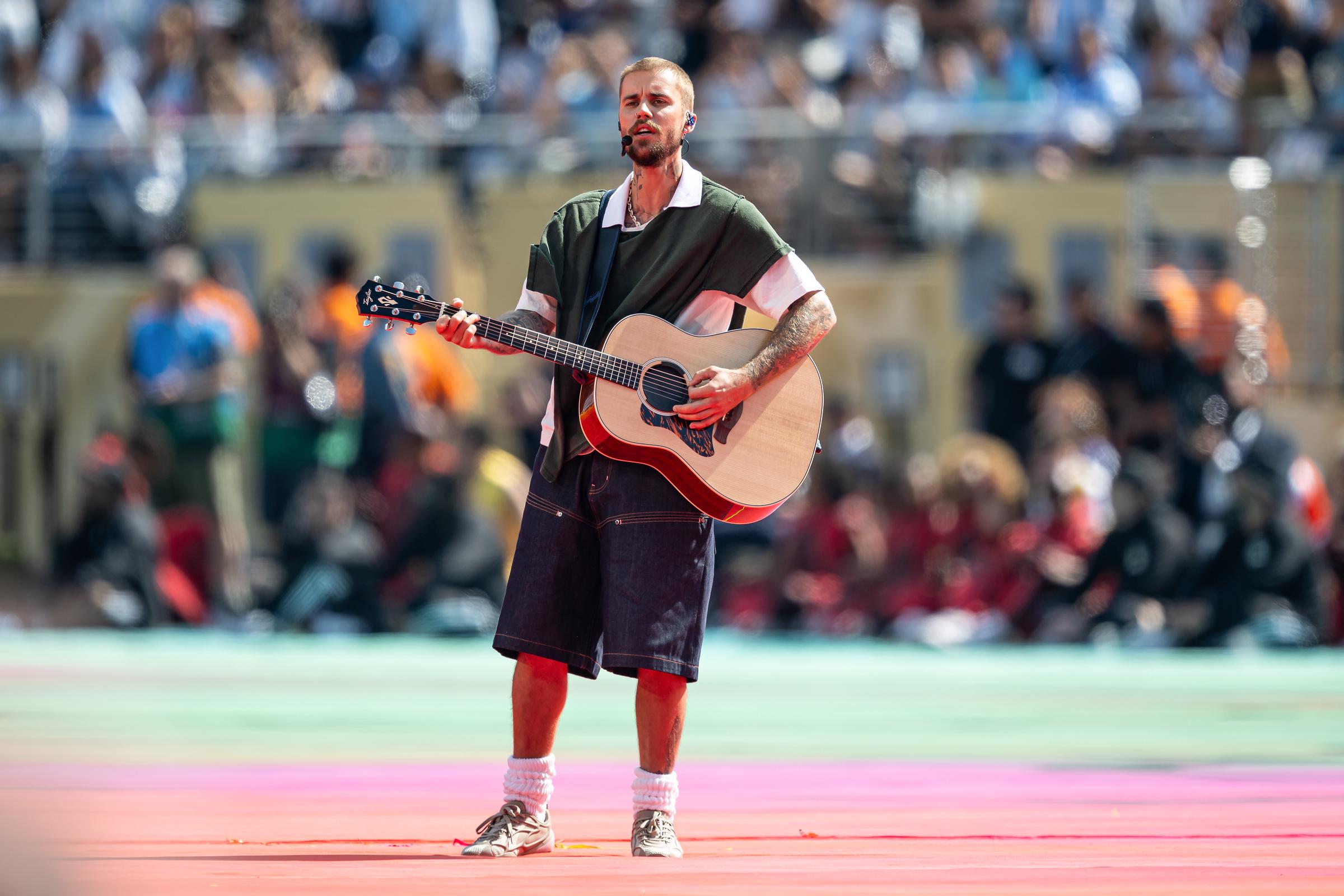 Justin Bieber performs his acoustic rendition of "Everything Hallelujah" at the World Cup Final, sporting the custom SKYLRK green deconstructed shirt and baggy denim shorts that fans quickly labeled a "homeless pancho fit." | Source: Getty Images