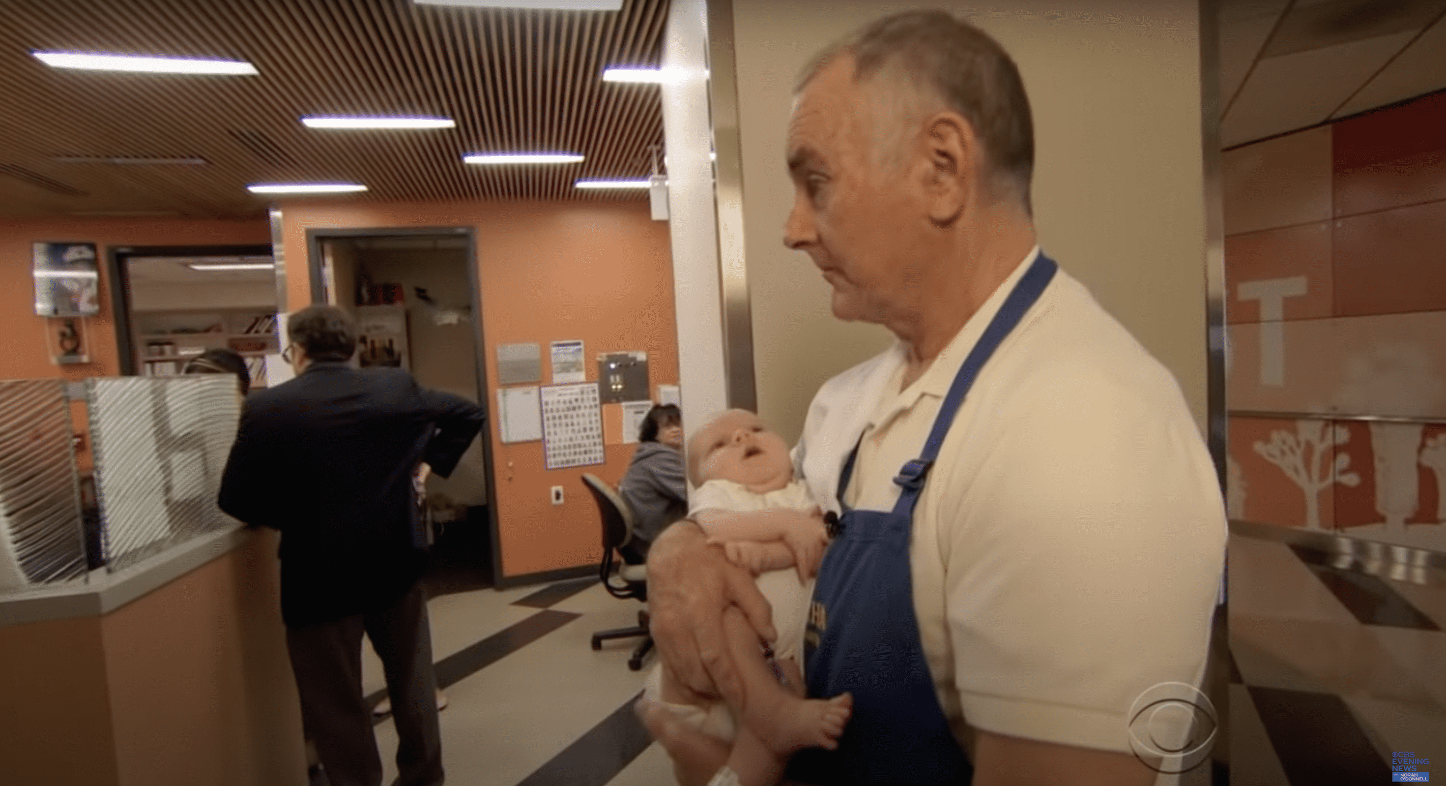 Jim O'Connor pictured cuddling a baby. | Source: youtube.com/CBS Evening News
