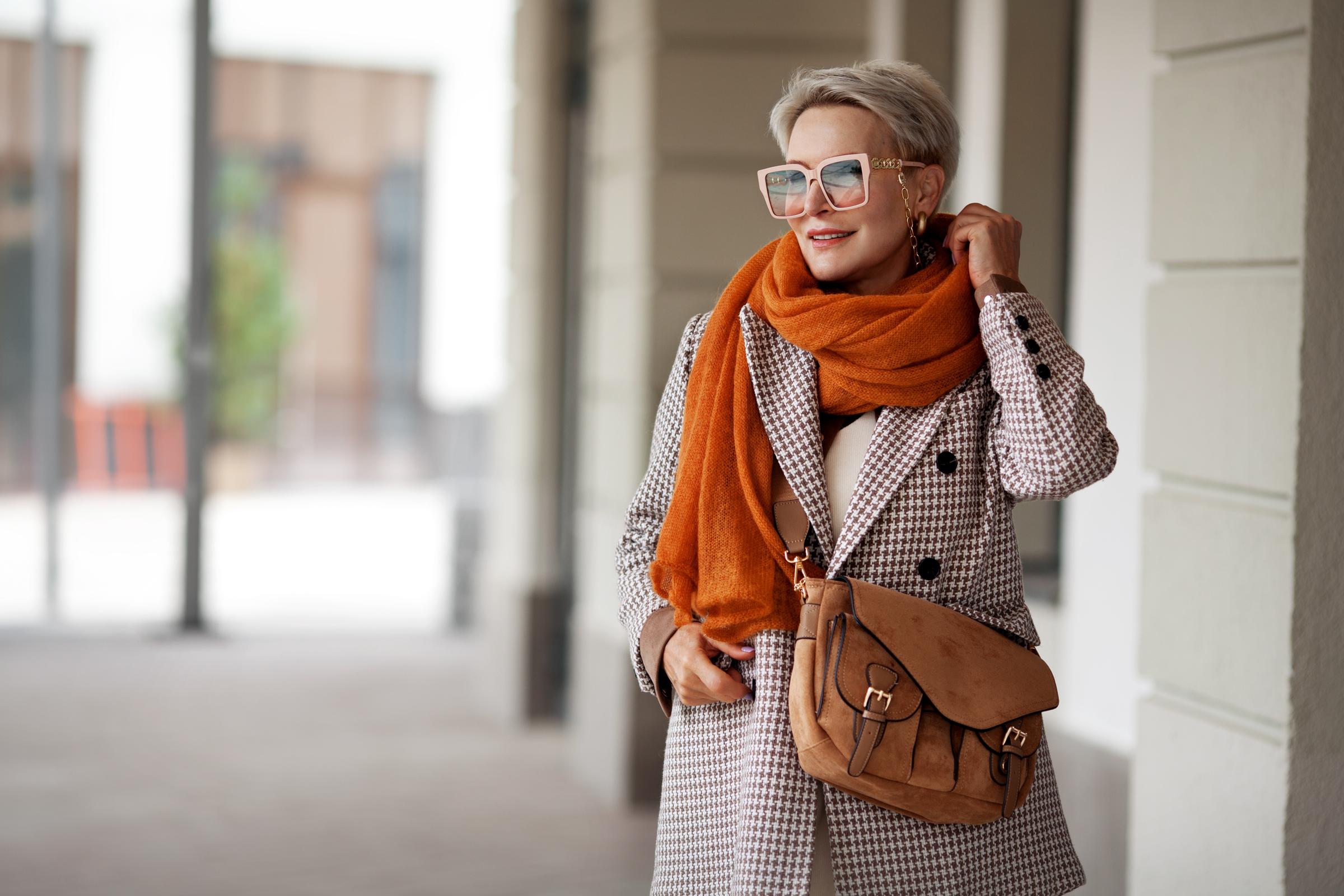Woman fashionably dressed for winter in a plaid coat rust scarf | Source: Shutterstock