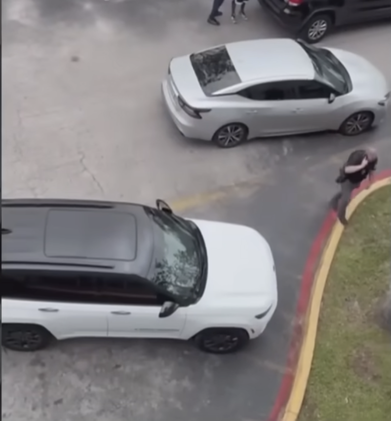 A wider view of the parking area shows multiple vehicles, including a white SUV and a sedan, as a person moves quickly along the curb, adding to the sense of urgency at the scene. | Source: YouTube/WPLG Local 10