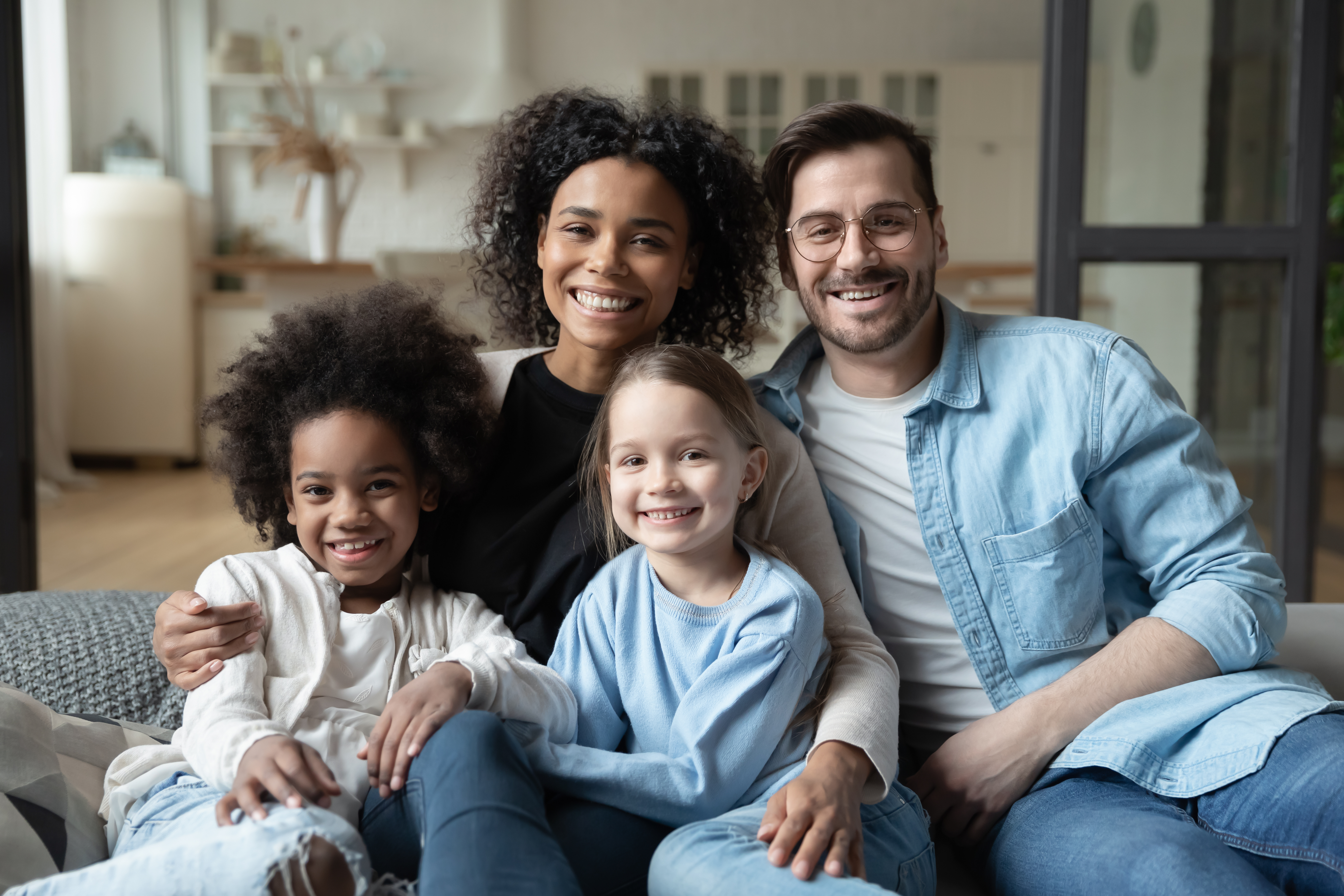 A multiracial couple smiling while sitting on a couch with their daughters | Source: Shutterstock