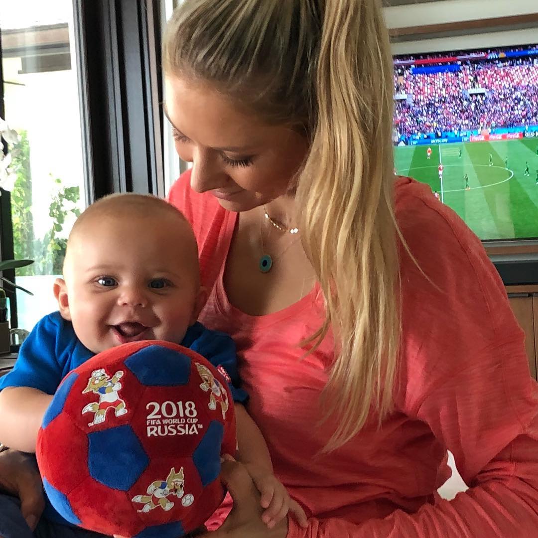 Anna Kournikova holding Nicholas Iglesias while a soccer game plays in the background, from a post dated June 14, 2018 | Source: Instagram/annakournikova