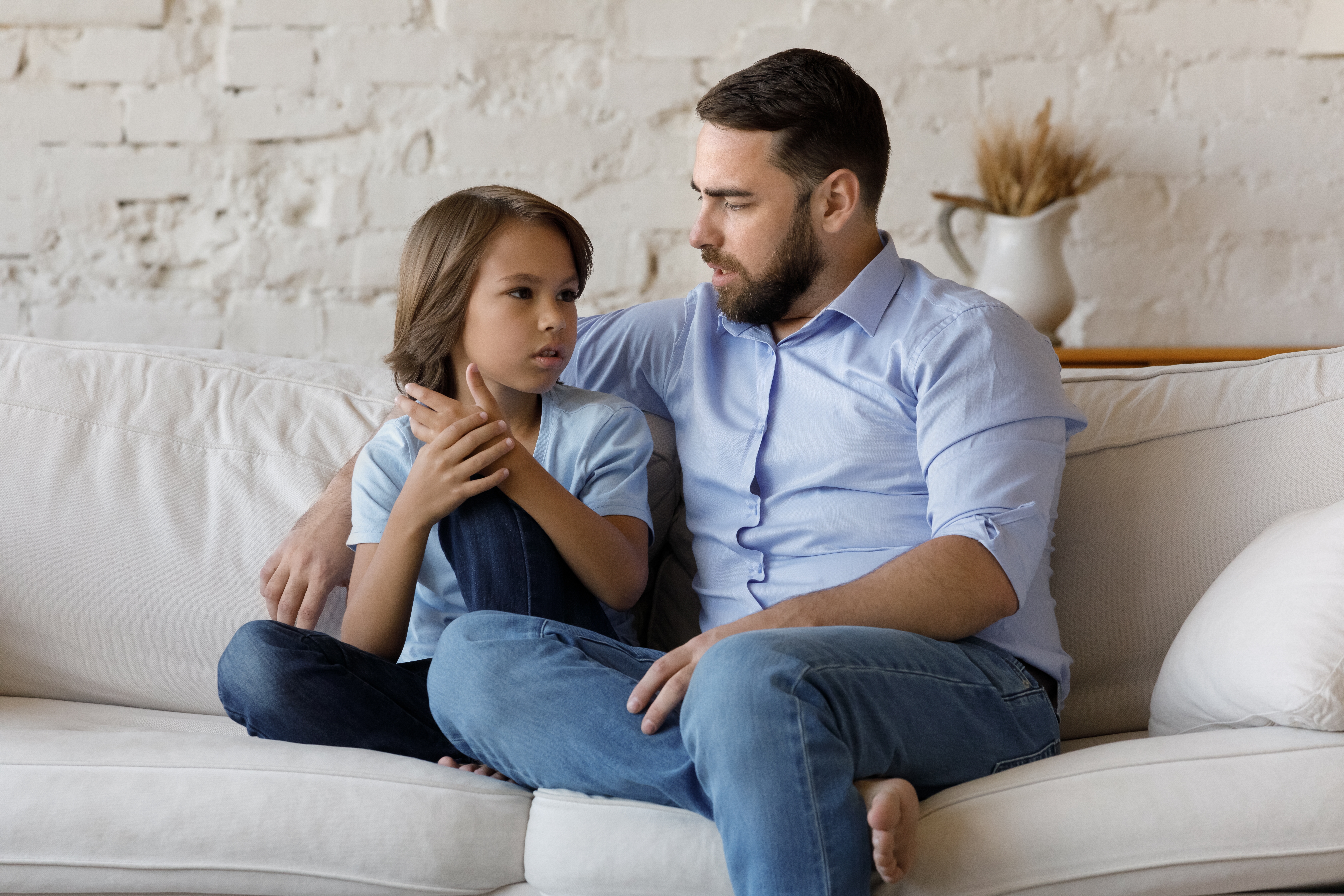 A serious father listens to his pre-teen son while sitting on a sofa at home | Source: Shutterstock