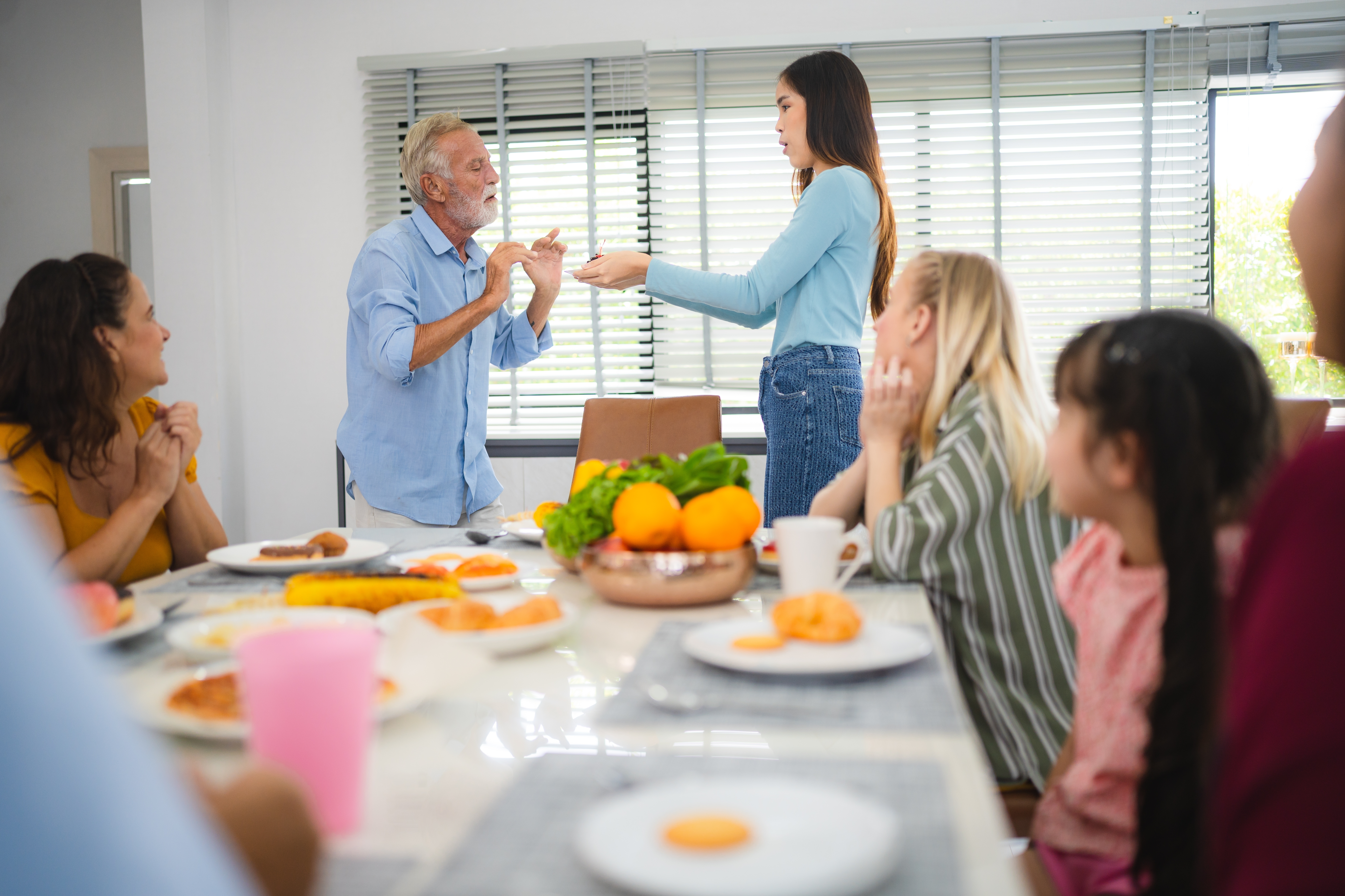 A senior man talking to a young girl during family dinner in the dining room | Source: Shutterstock