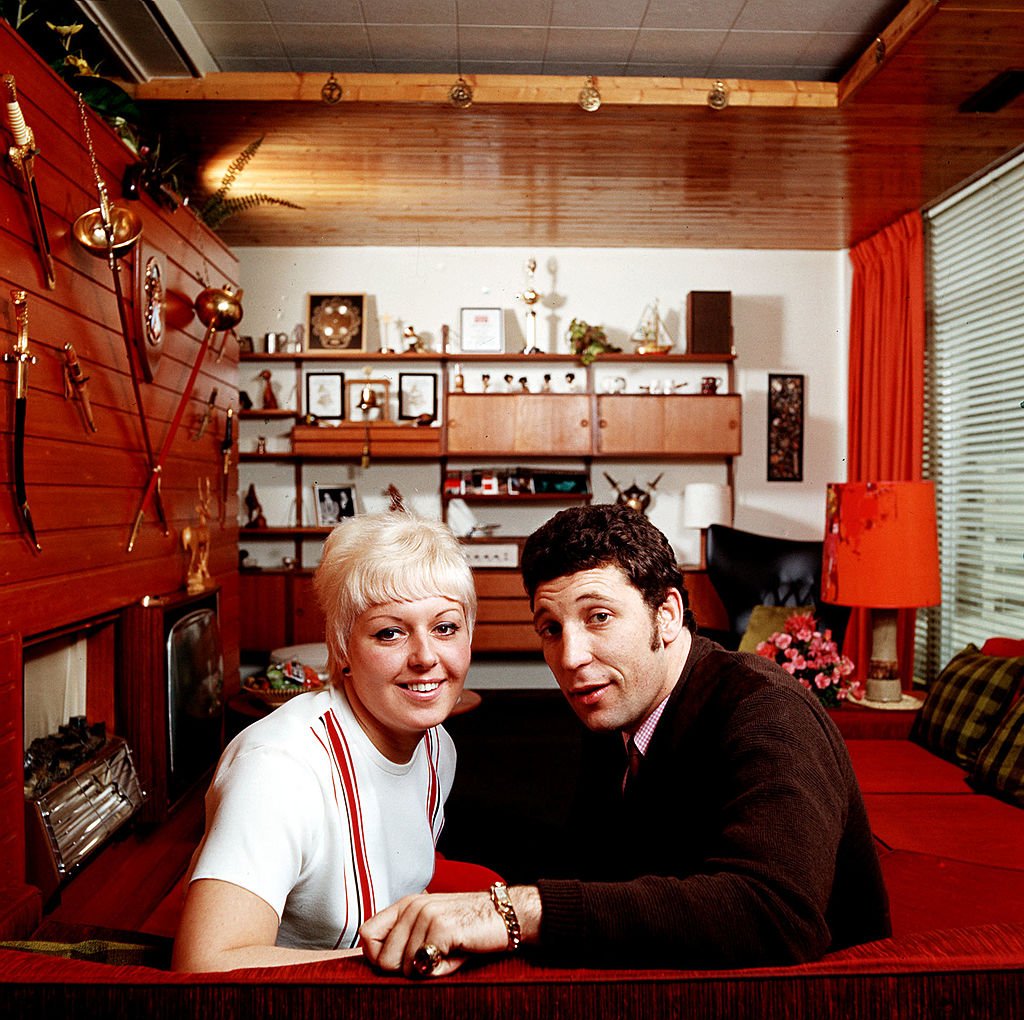 Tom Jones and Melinda Trenchard posing while seated on a couch at home. / Source: Getty Images