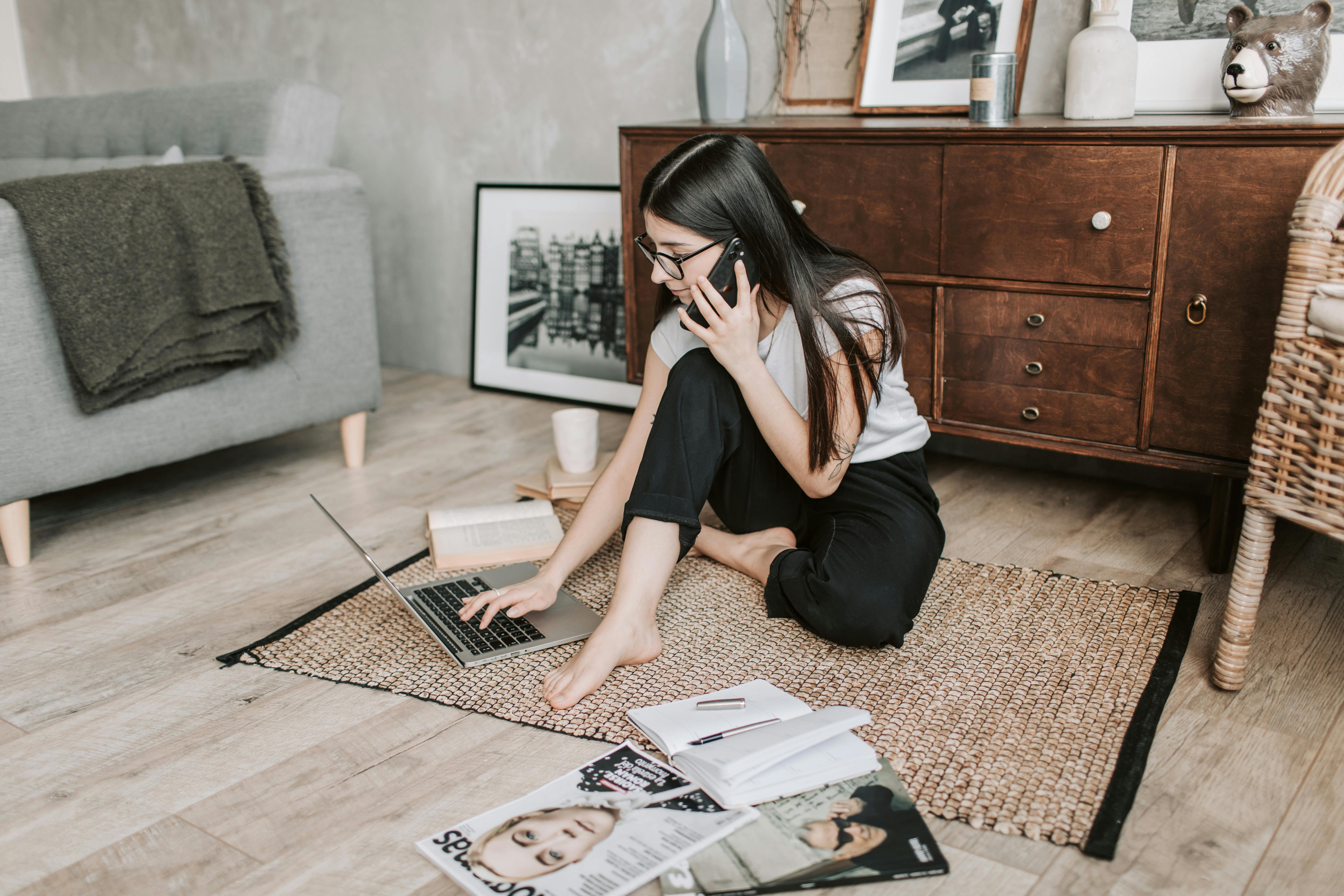 A young girl on the phone with a laptop, books, and magazines around her | Source: Pexels