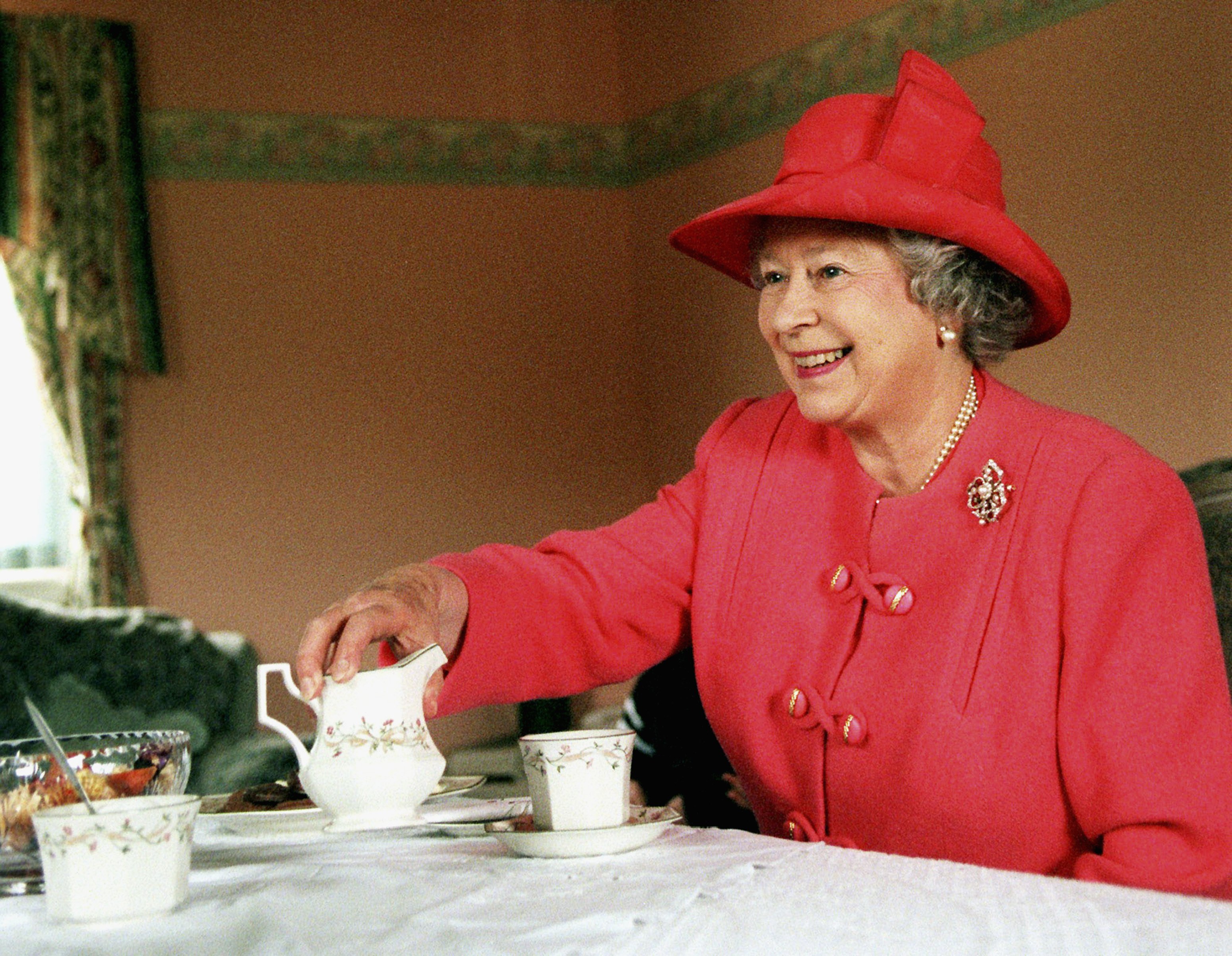 Queen Elizabeth II joins Mrs Susan McCarron, her ten-year-old son, James, and Housing Manager Liz McGinniss for tea in their home in the Castlemilk area of Glasgow in Scotland on July 7, 1999. | Source: Getty Images