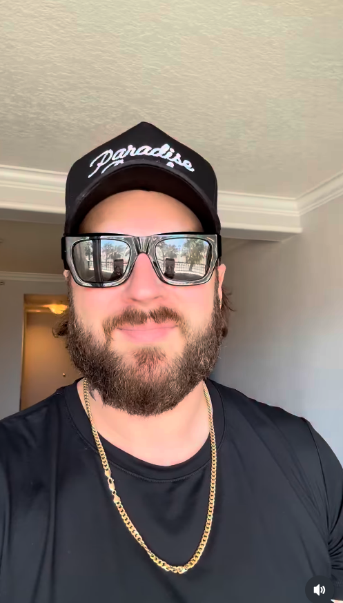 Nate Smith looks directly into the camera for a close-up selfie, sporting a full beard, oversized dark sunglasses, a black “Paradise” cap, and a gold chain. | Source: Instagram/natesmith