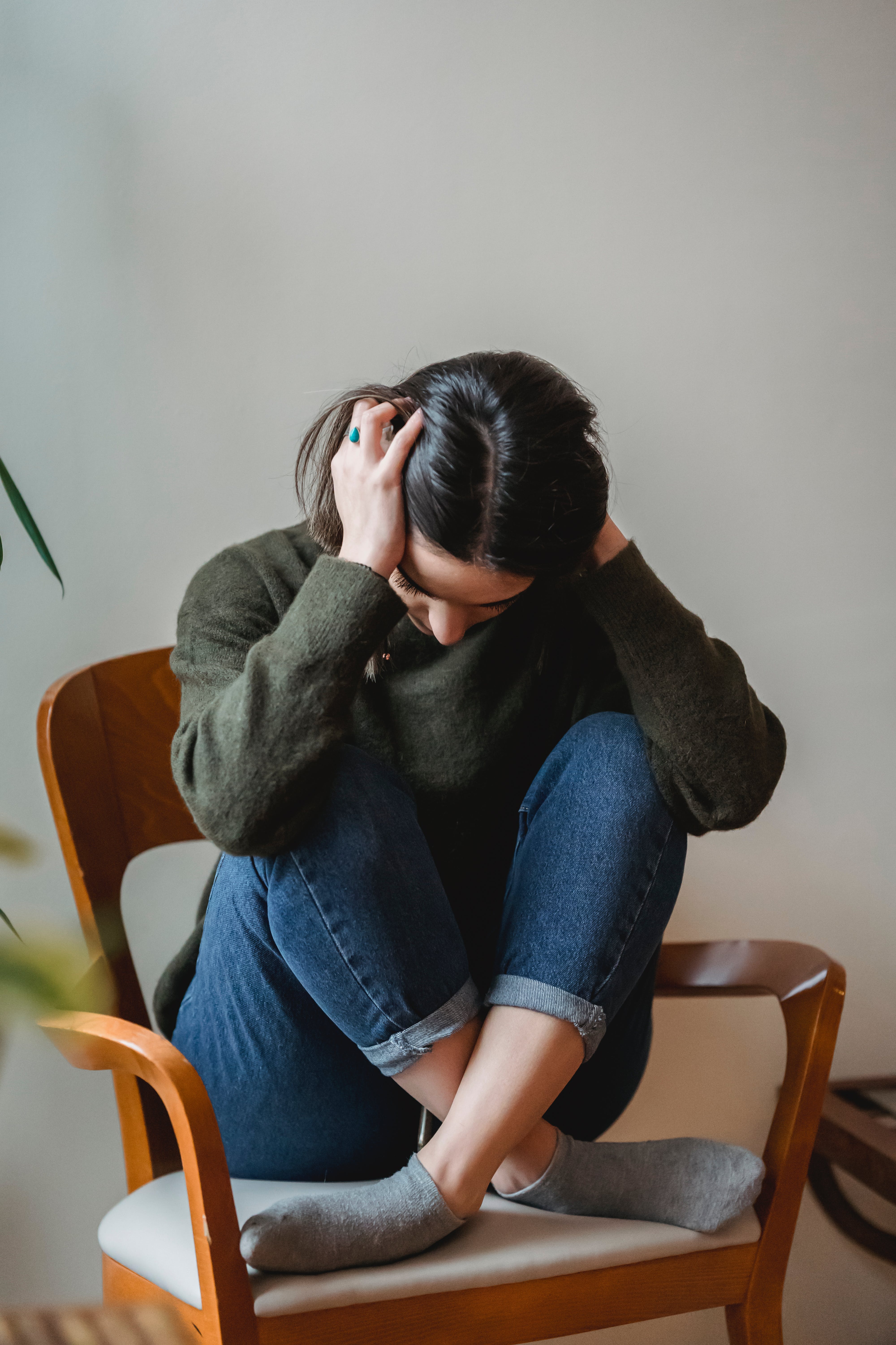 An upset woman sitting cross-legged on a chair while holding her head with her hands | Source: Pexels