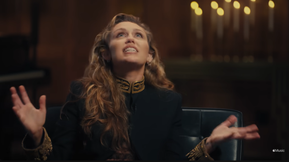 Miley Cyrus gestures expressively during her Apple Music interview, opening up about the personal cost behind her vocal strength | Source: YouTube/AppleMusic