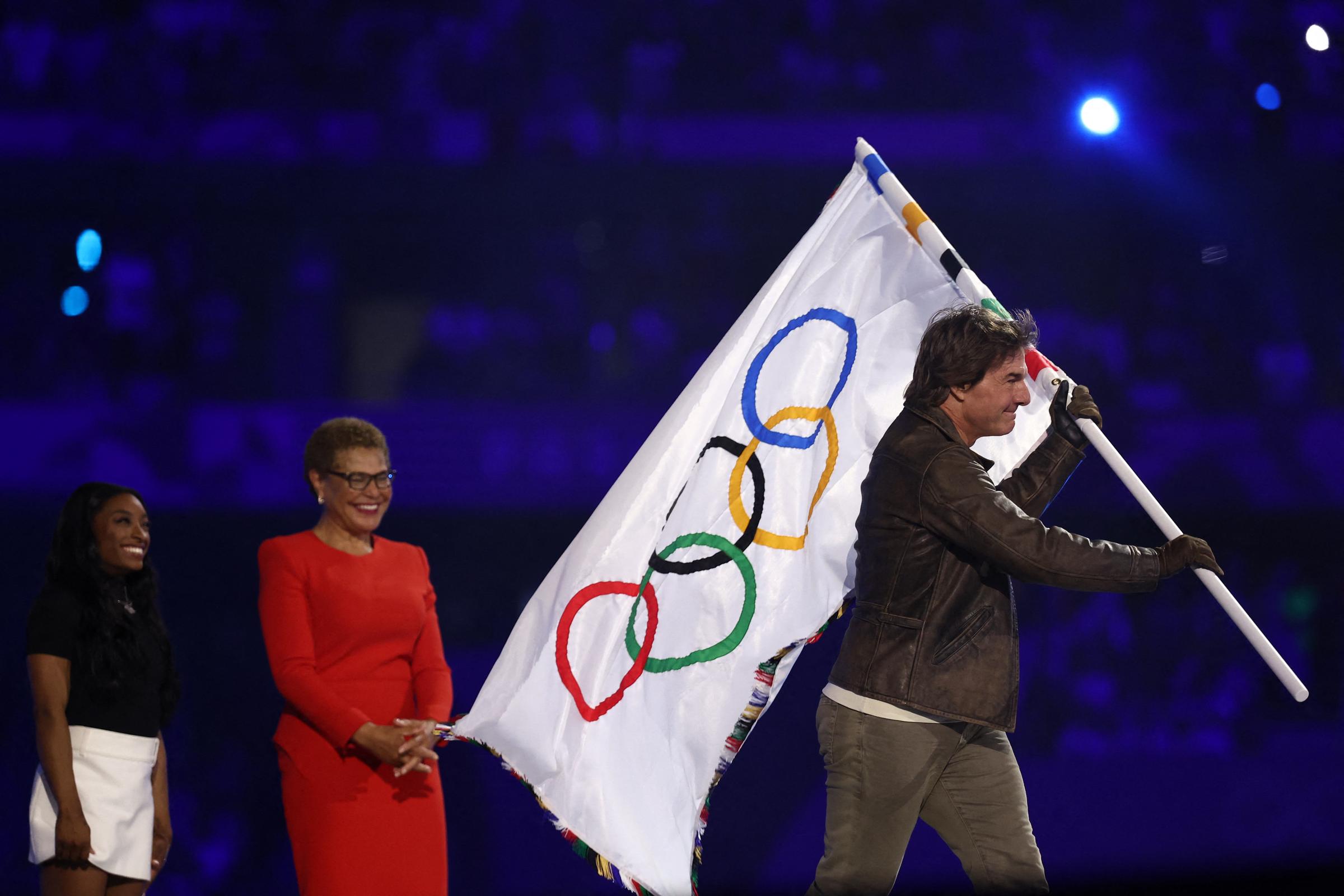 Simone Biles and Karen Bass watches Tom Cruise as he walks away with the Olympic flag | Source: Getty Images