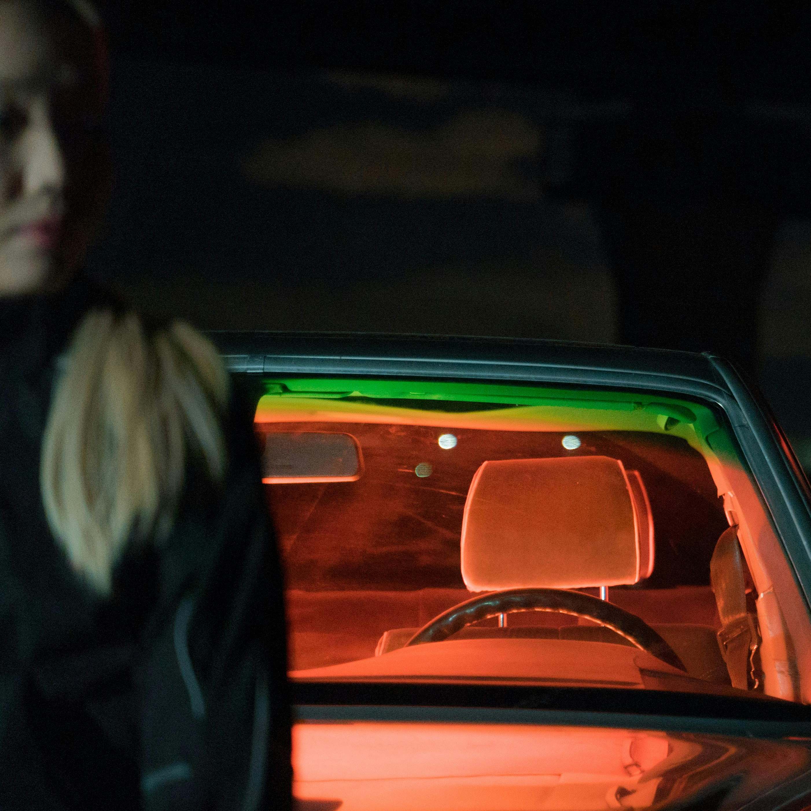 A woman near a parked car at night | Source: Midjourney