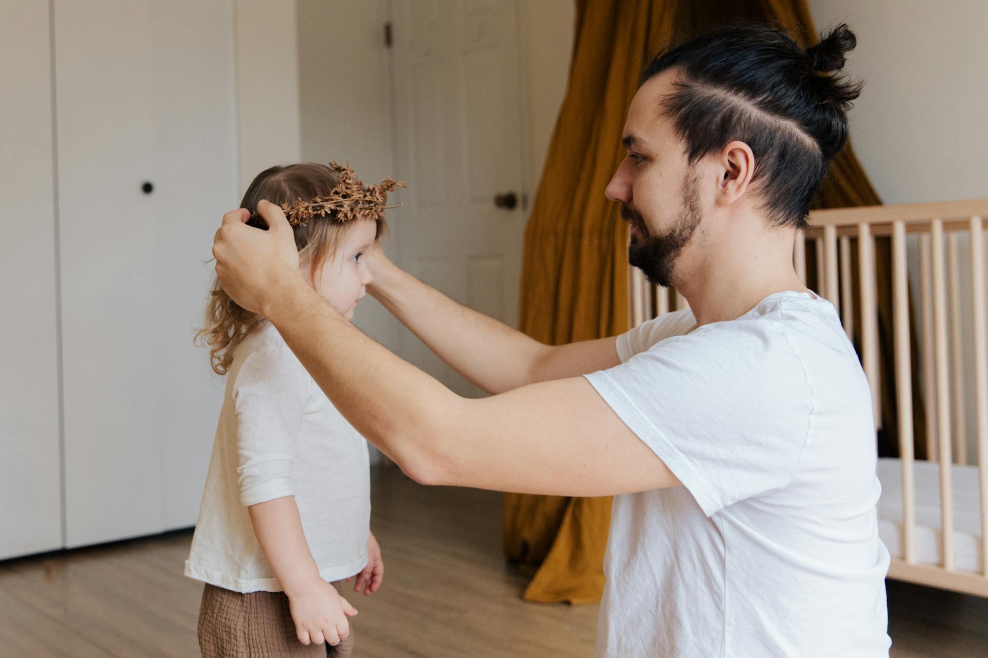 A man putting a flower crown on his daughter's head | Source: Pexels