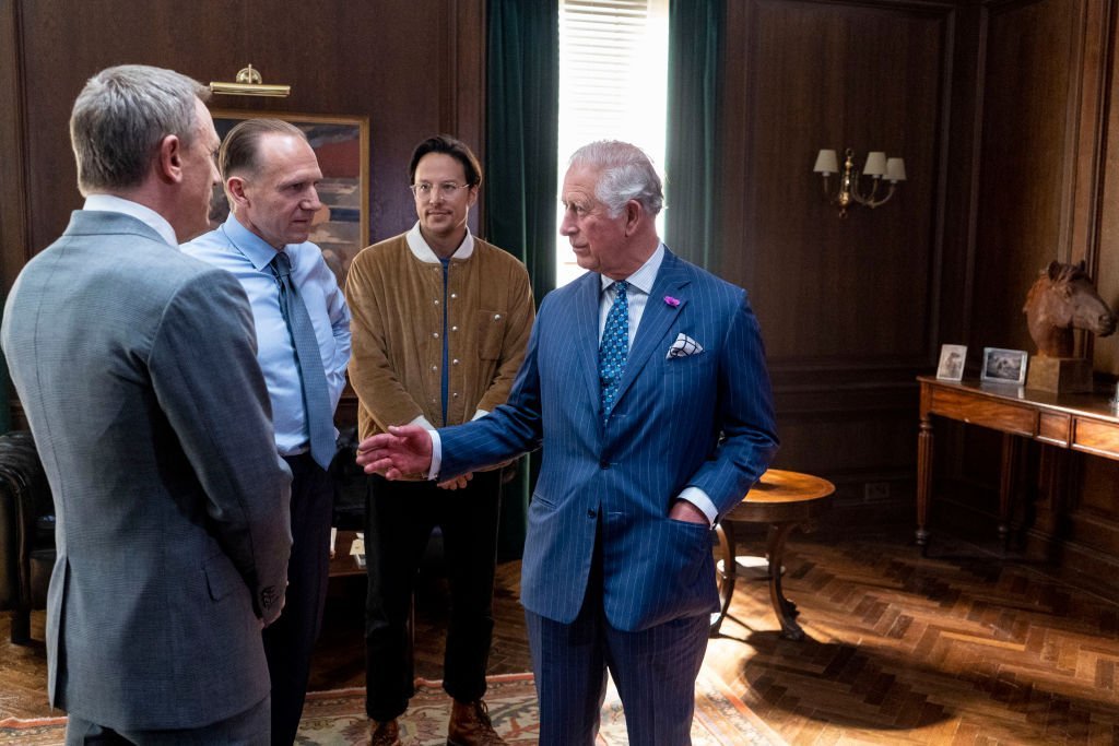 Prince charles speaks to actors Ralph Fiennes, Daniel Craig, and Director Cary Joji Fukunaga during a tour of the new "James Bond" film set in June 2019 | Photo: Getty Images