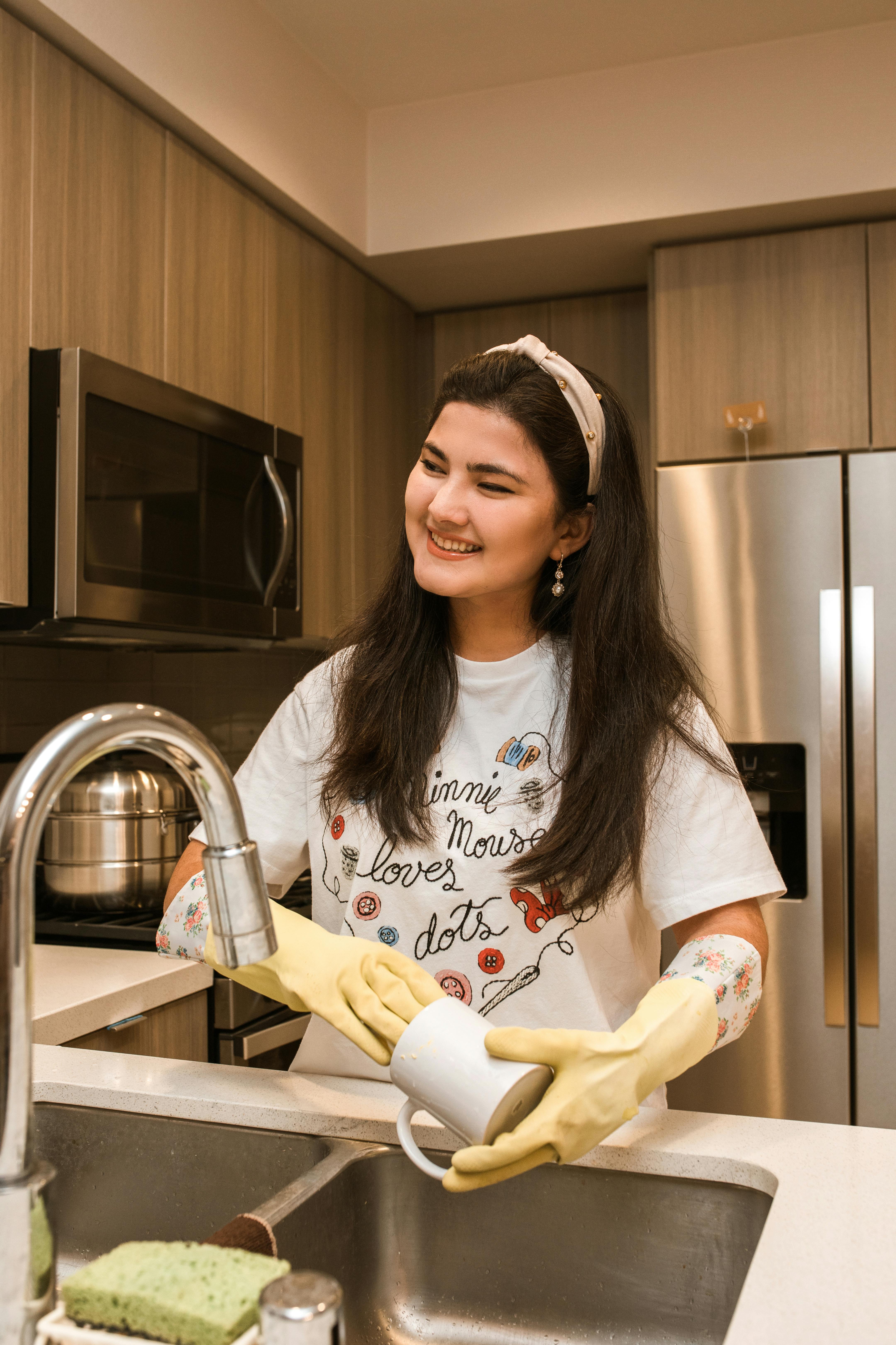 A woman smiling while washing dishes | Source: Pexels