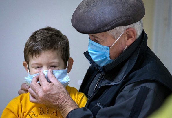 Un homme aide un enfant à mettre un masque de protection.| Photo : Getty Images